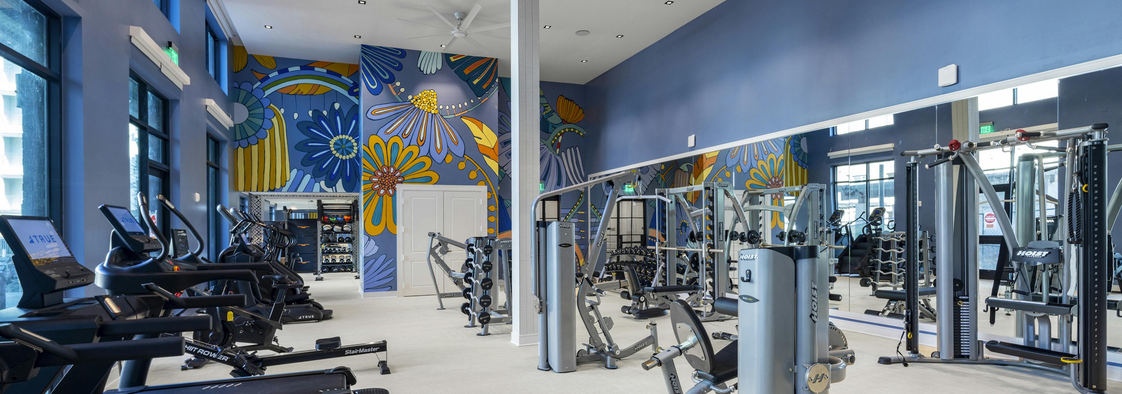 Fitness center at AMLI North Park with treadmills, strength training equipment, large mirrors, and a vibrant floral mural on a blue wall