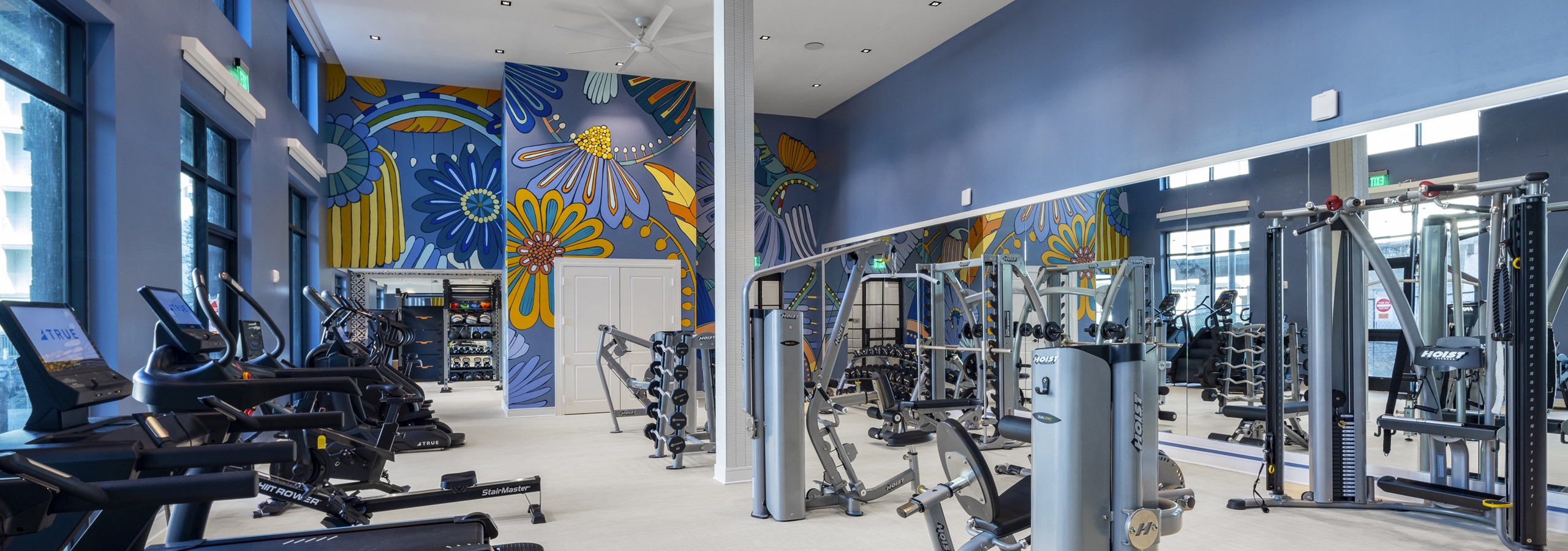 Fitness center at AMLI North Park with treadmills, strength training equipment, large mirrors, and a vibrant floral mural on a blue wall