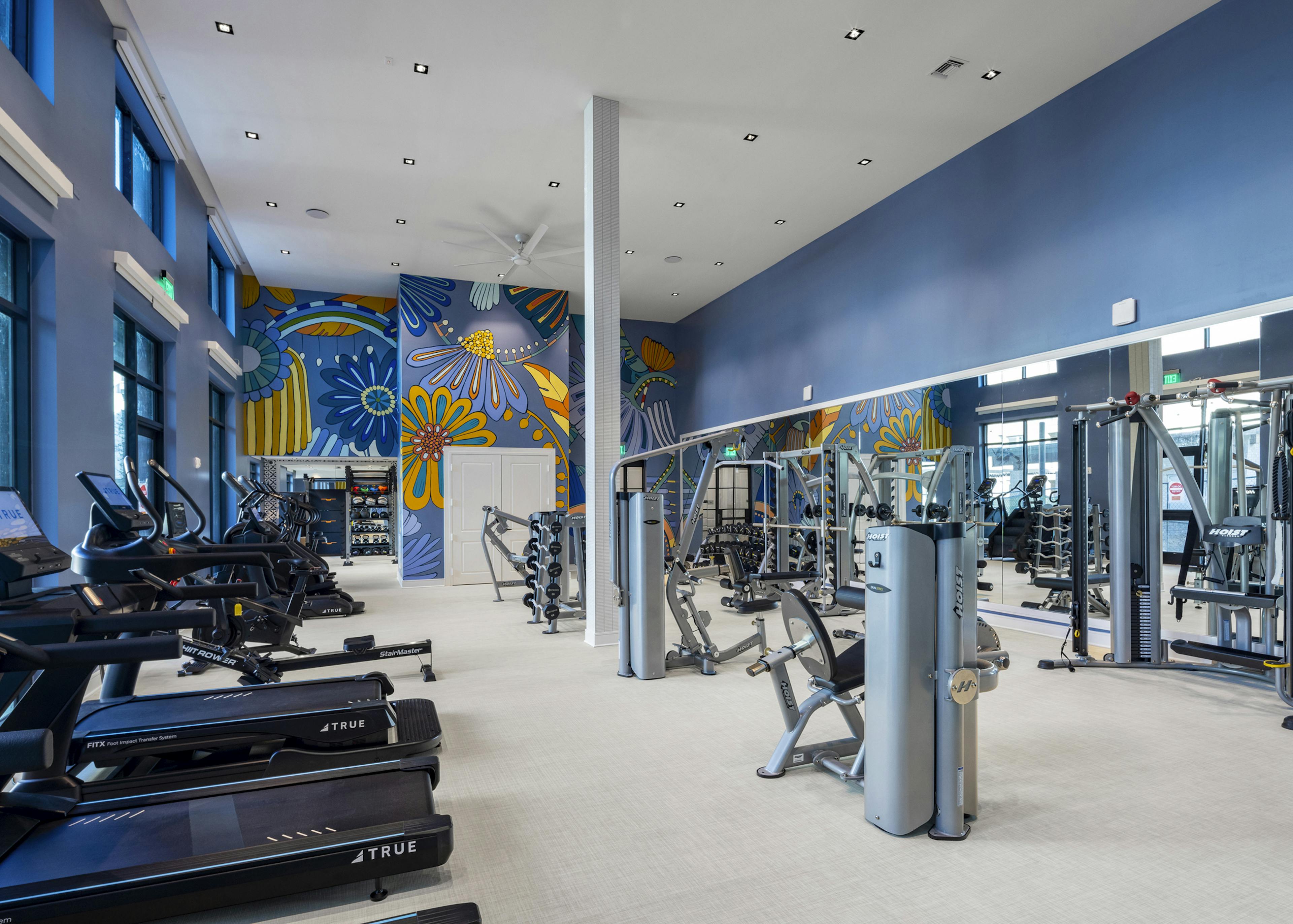 Fitness center at AMLI North Park with treadmills, strength training equipment, large mirrors, and a vibrant floral mural on a blue wall