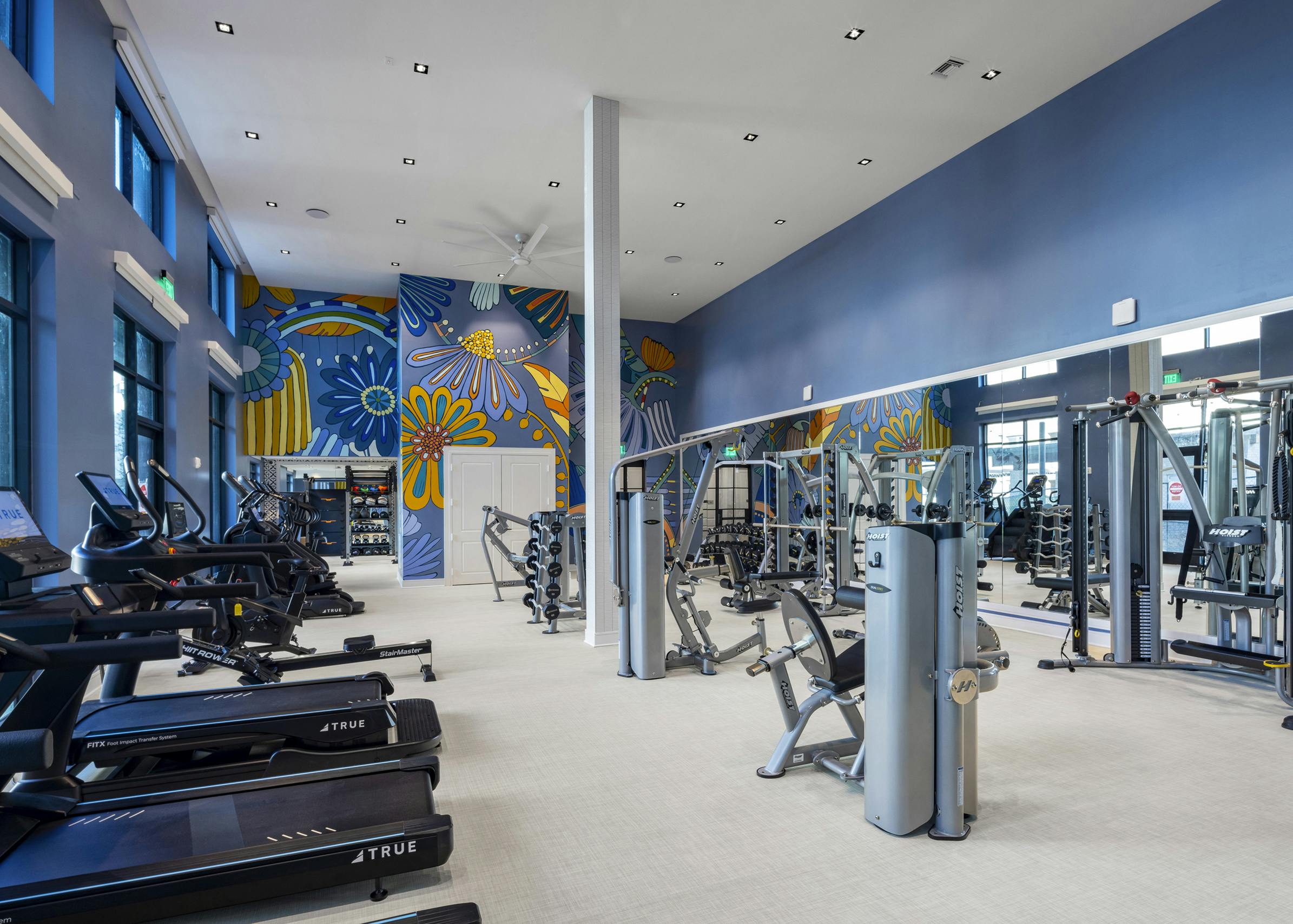 Fitness center at AMLI North Park with treadmills, strength training equipment, large mirrors, and a vibrant floral mural on a blue wall