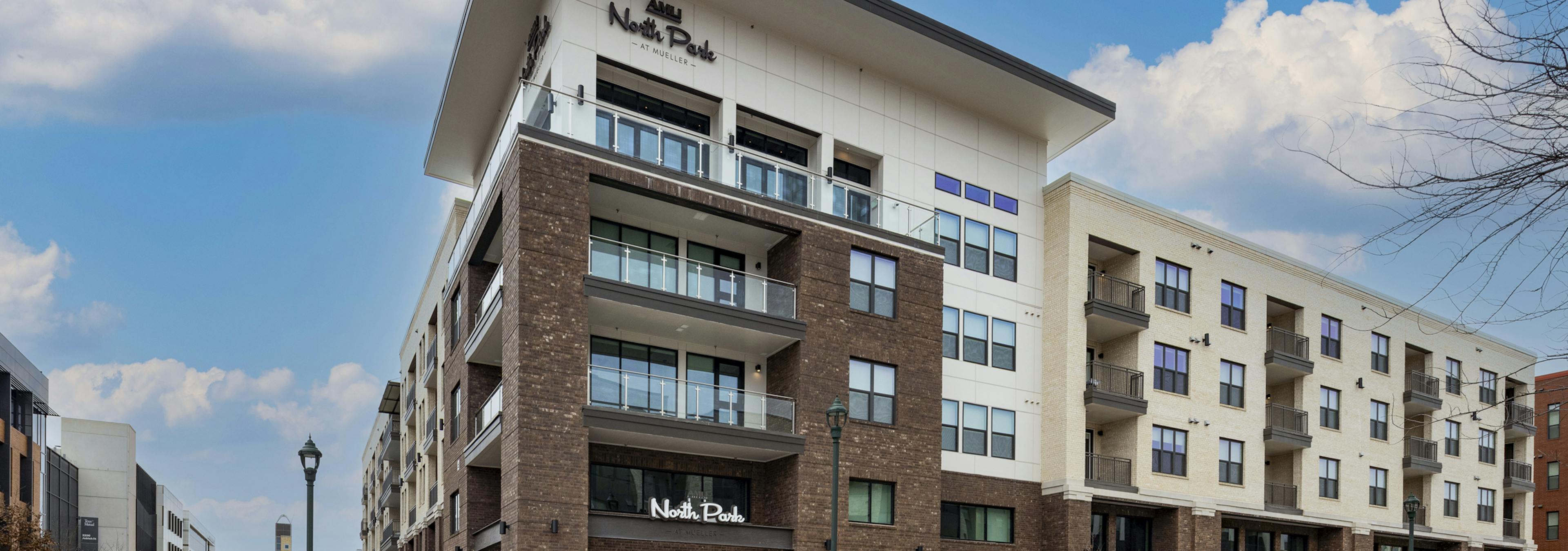 Exterior daytime view of AMLI North Park apartments with a brick and white facade, private balconies, and large windows under a blue sky