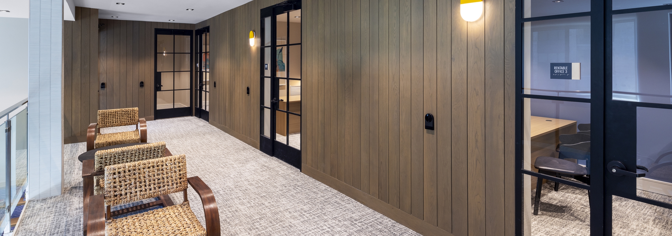View of private office at AMLI North Park with glass office doors, woven chairs, wood-paneled walls, and modern lighting