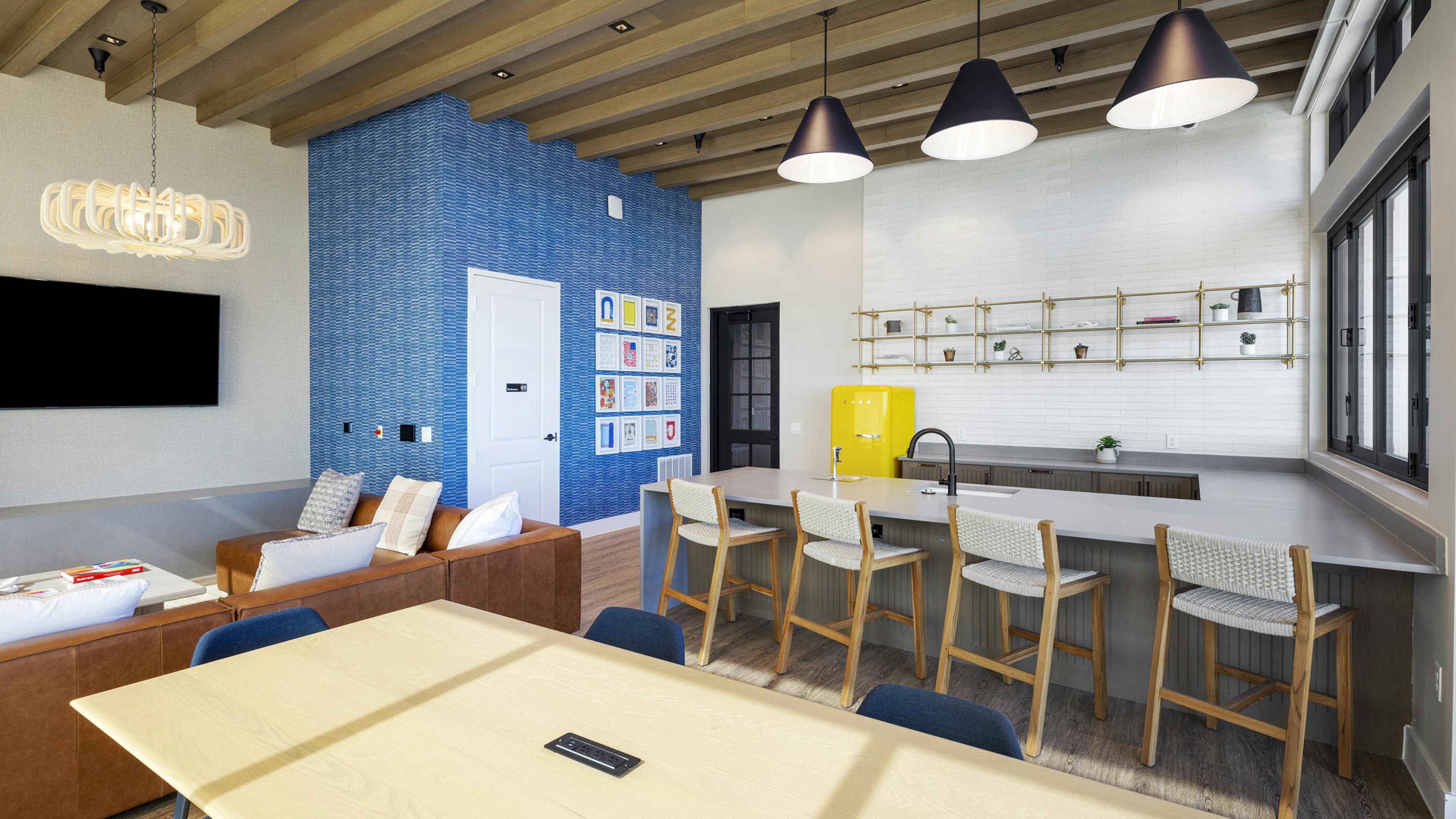 Resident lounge at AMLI North Park with a kitchenette, barstools, a blue accent wall, and a cozy seating area with a leather sofa