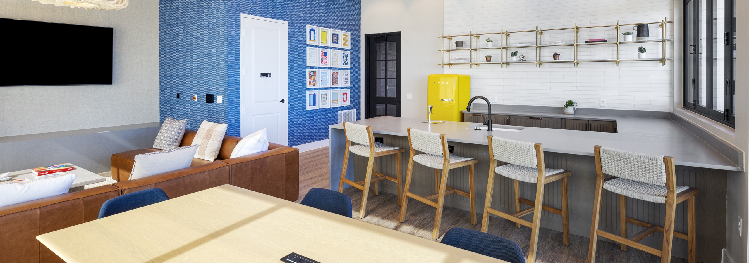 Resident lounge at AMLI North Park with a kitchenette, barstools, a blue accent wall, and a cozy seating area with a leather sofa