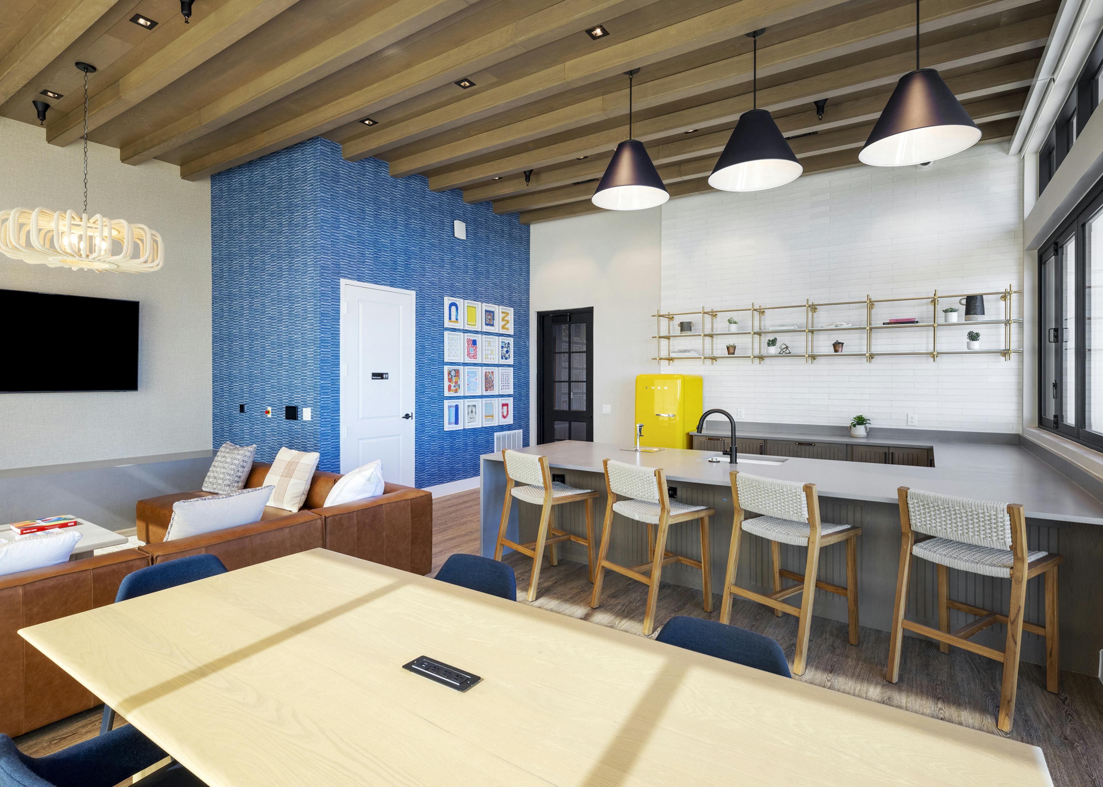 Resident lounge at AMLI North Park with a kitchenette, barstools, a blue accent wall, and a cozy seating area with a leather sofa