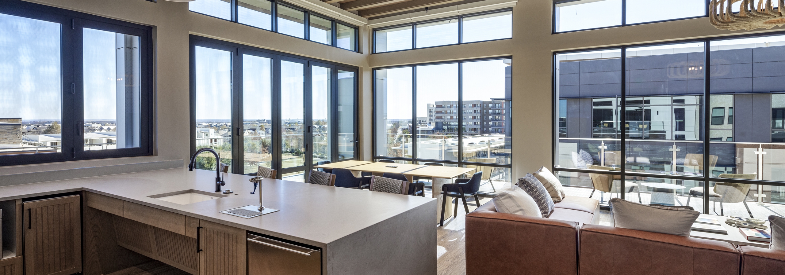 Rooftop lounge at AMLI North Park with a modern kitchen, bar seating, wood ceiling beams, and floor-to-ceiling windows with skyline views