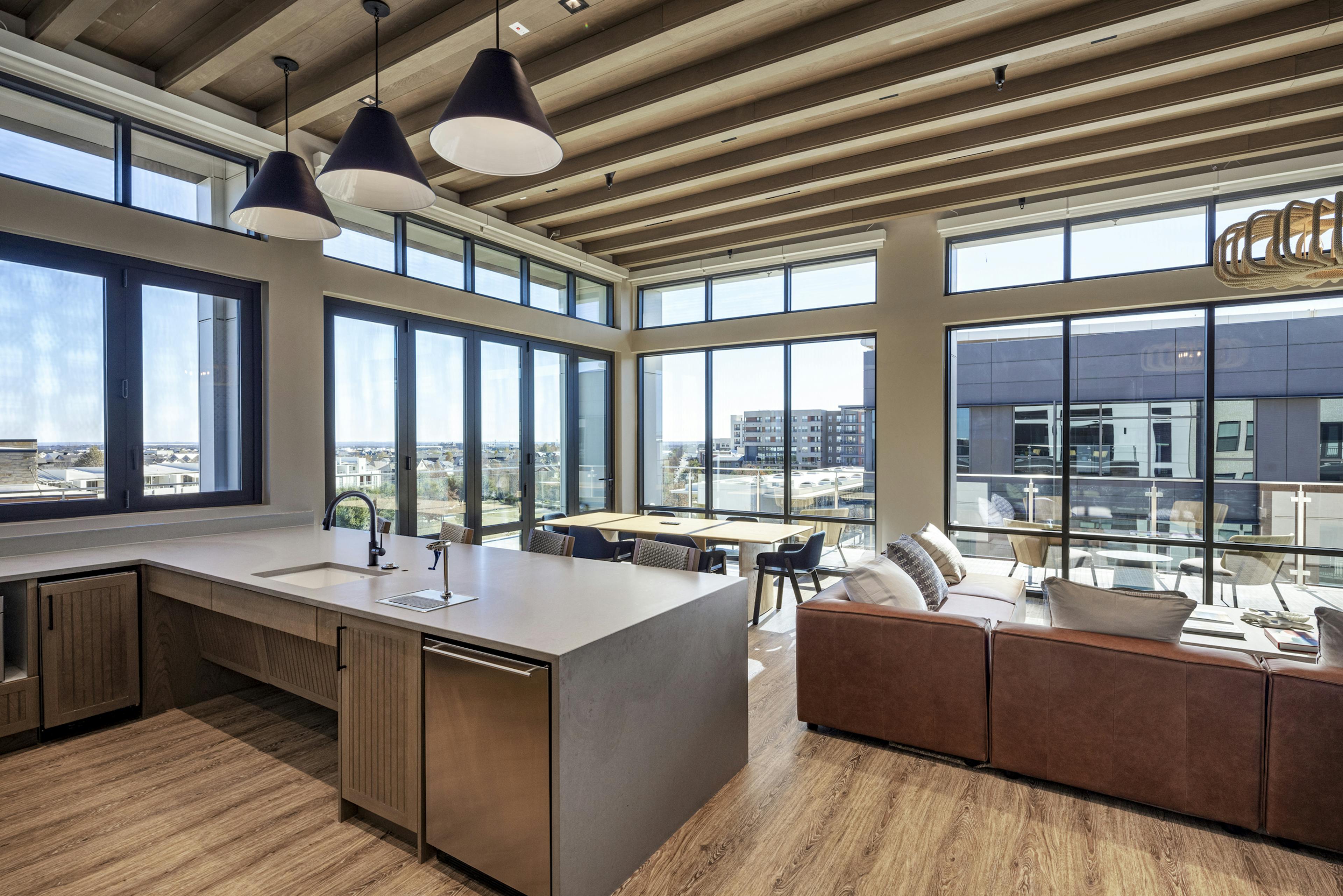Rooftop lounge at AMLI North Park with a modern kitchen, bar seating, wood ceiling beams, and floor-to-ceiling windows with skyline views