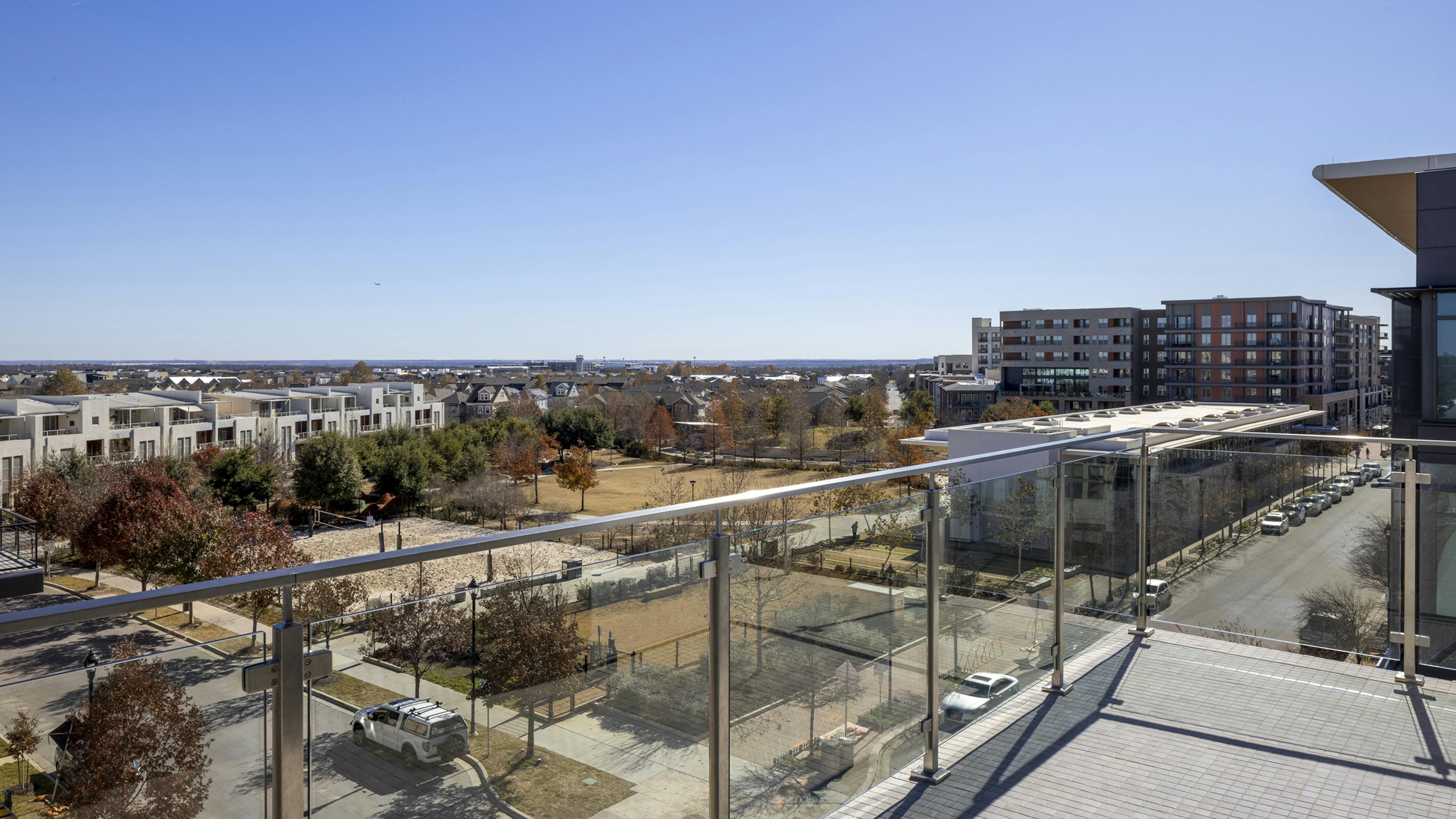 Scenic rooftop terrace at AMLI North Park with a glass railing, overlooking a park, modern townhomes, and city buildings in the distance