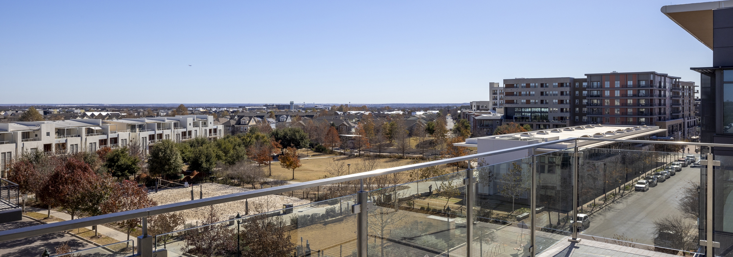 Scenic rooftop terrace at AMLI North Park with a glass railing, overlooking a park, modern townhomes, and city buildings in the distance