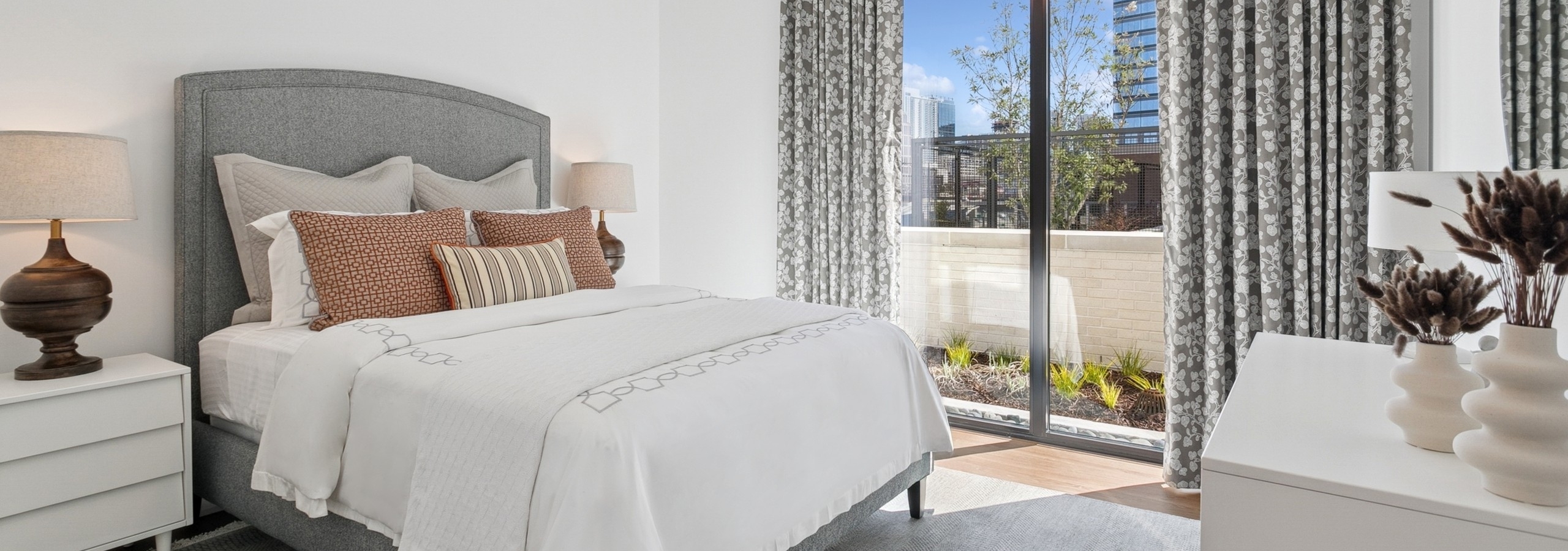 Interior view of a bedroom at AMLI Atlantic Station with queen bed with white blanket and patterned pillows and large window