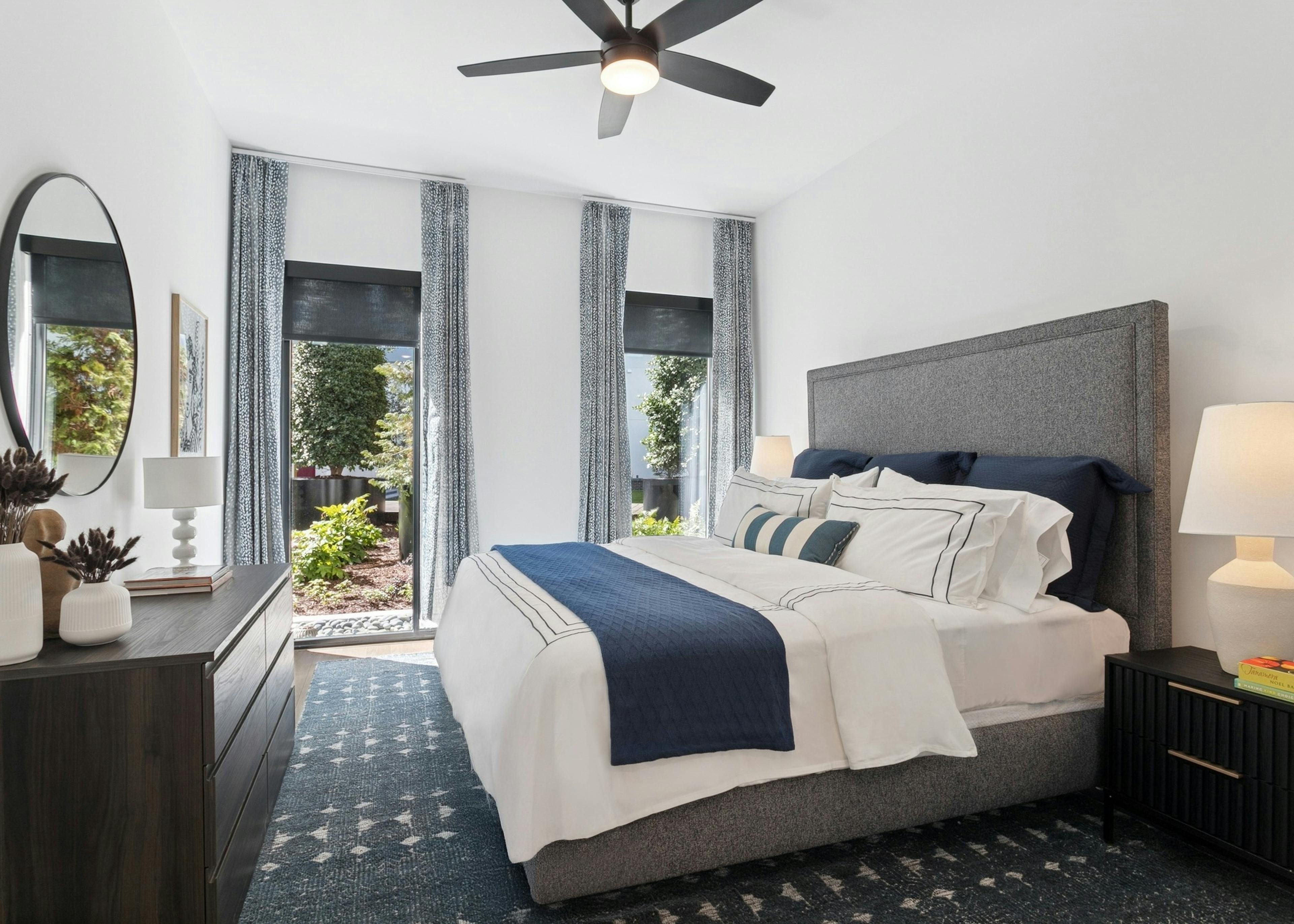 AMLI Atlantic Station apartment bedroom with a king gray upholstered bed with white and navy bedding and curtained windows
