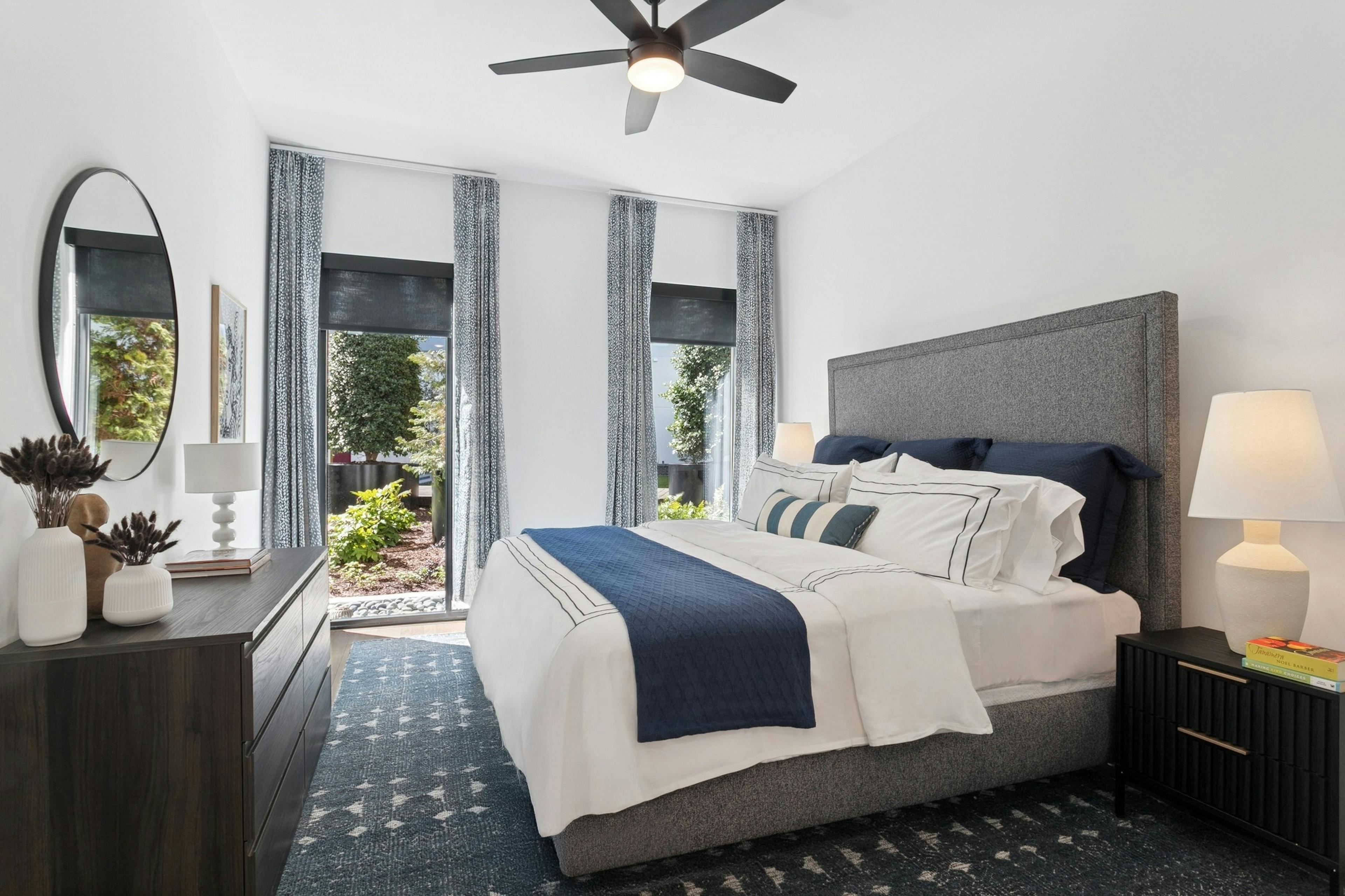 AMLI Atlantic Station apartment bedroom with a king gray upholstered bed with white and navy bedding and curtained windows