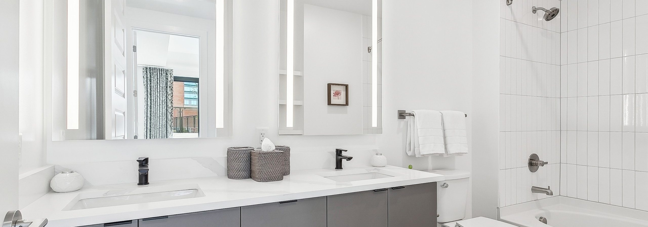 Contemporary bathroom at AMLI Atlantic Station featuring a sleek gray double vanity with mirrors above and a white bathtub