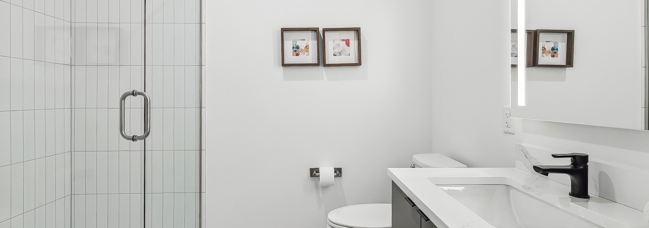 Bathroom at AMLI Atlantic Station apartments with a glass shower with white tiles and gray cabinetry with a mirror above