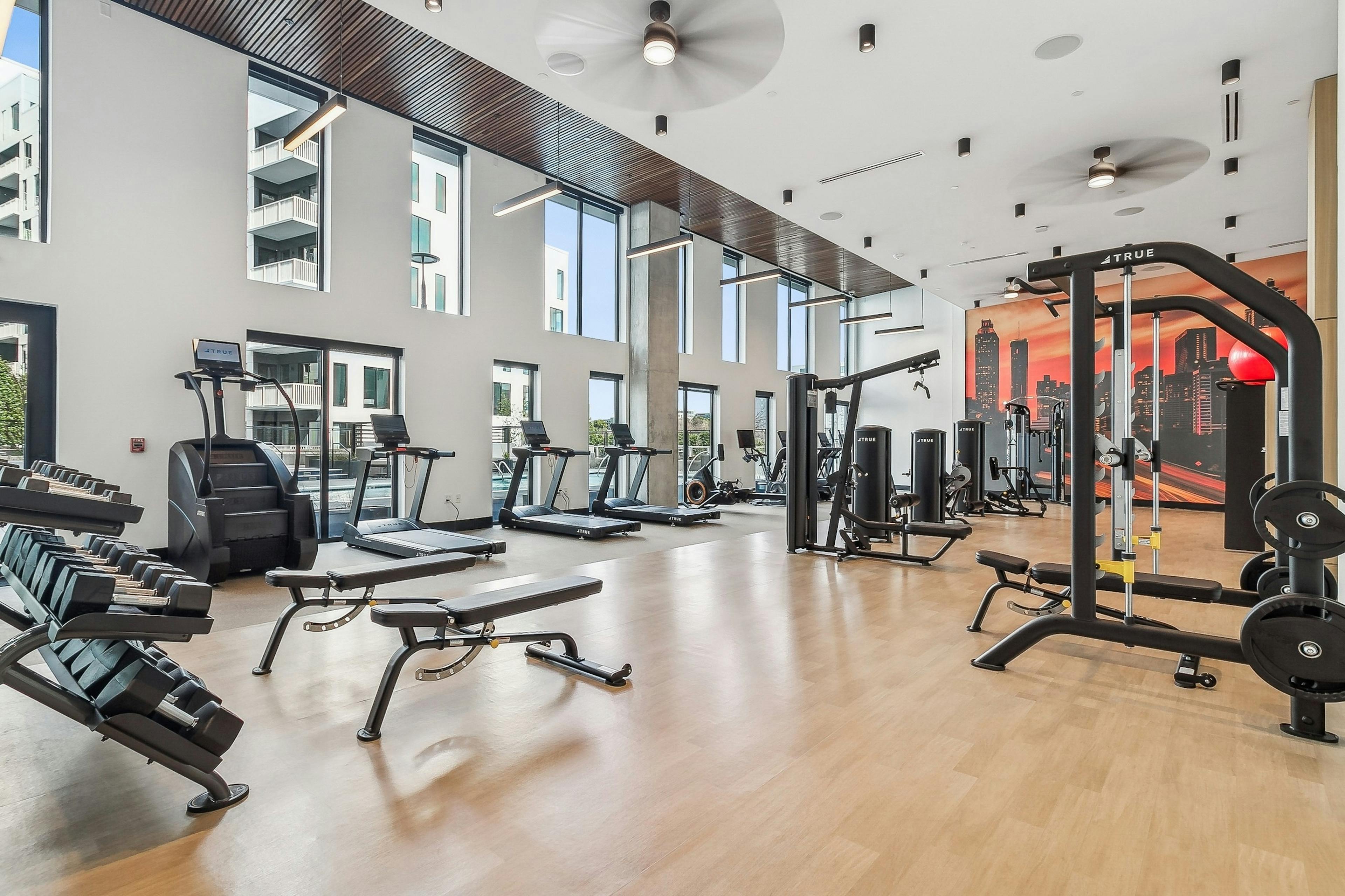 Interior view of a gym at AMLI Atlantic Station with large windows and treadmills and weight benches and a cable machine