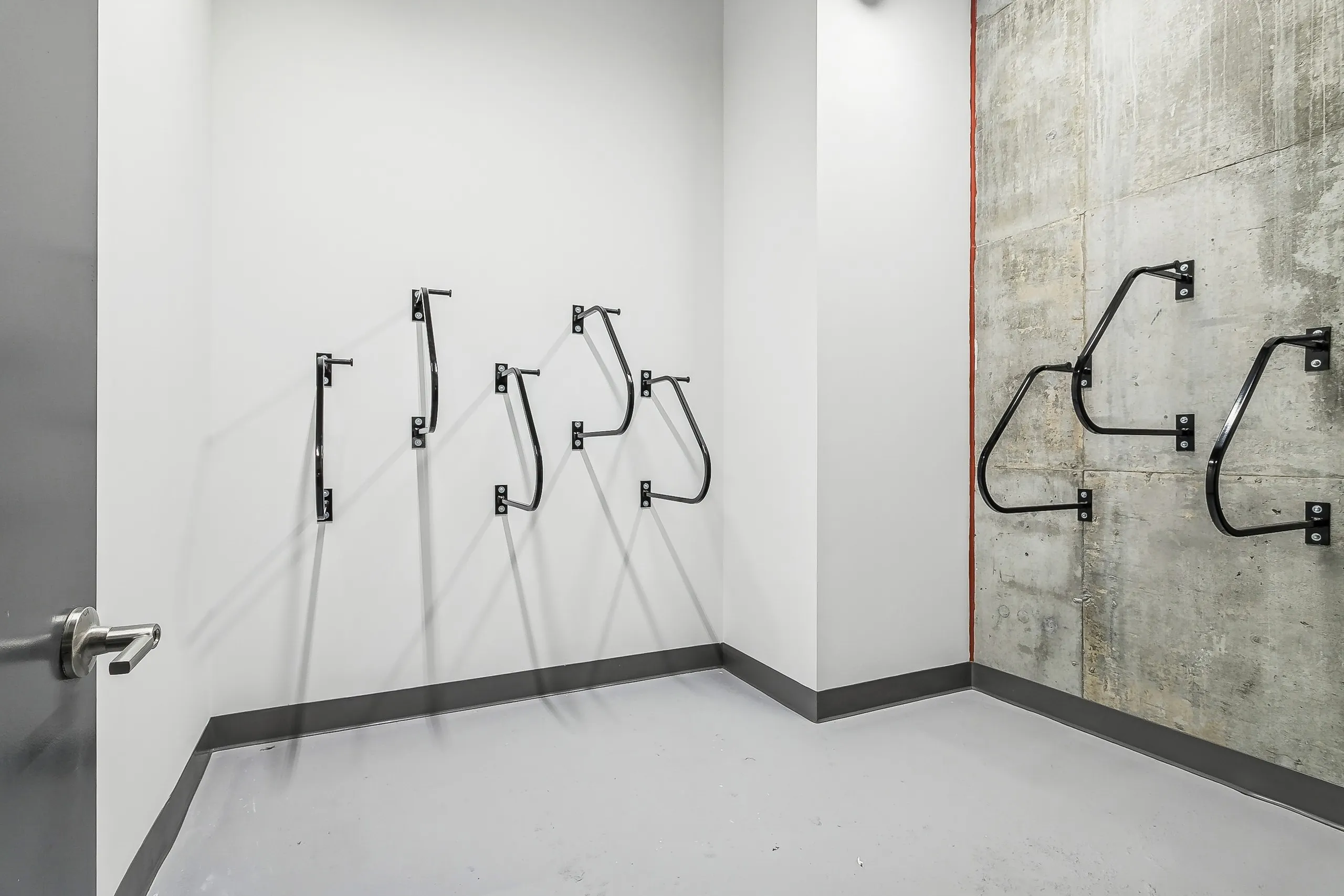 Minimalist bike storage room at AMLI Atlantic Station with several black wall mounted racks on white and gray concrete walls