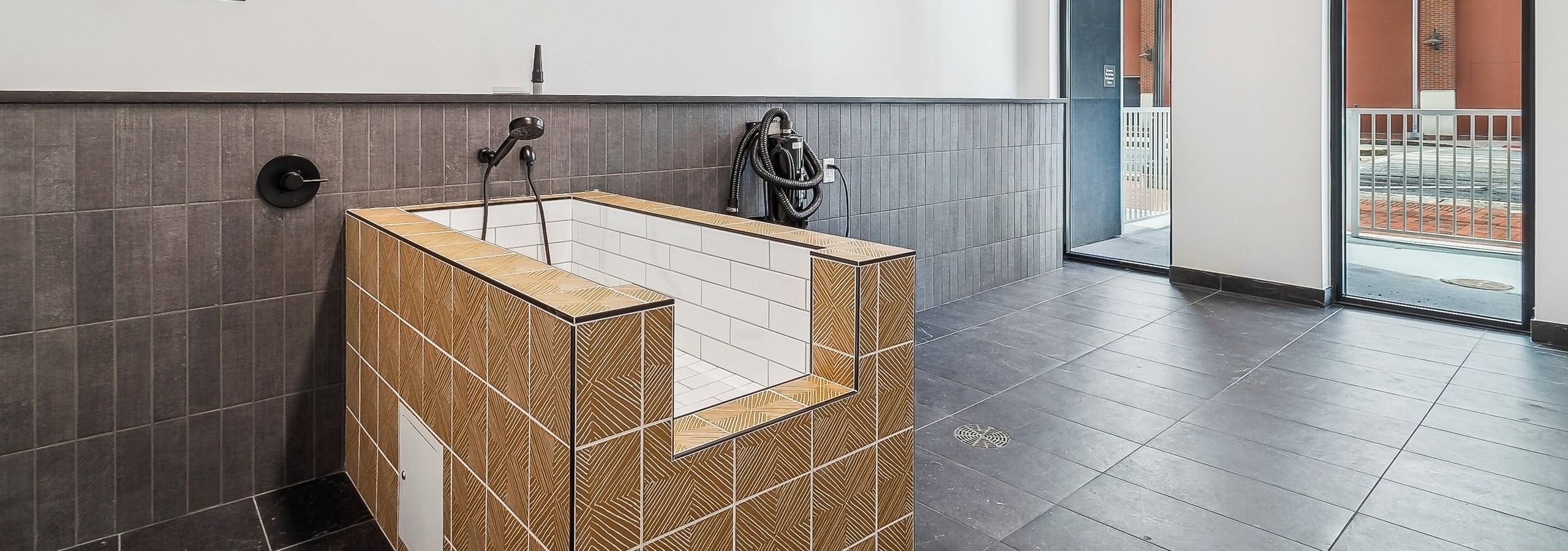 A pet washing station at AMLI Atlantic Station apartments with a tan and white tiled tub set on brown tiled floor and view to outside
