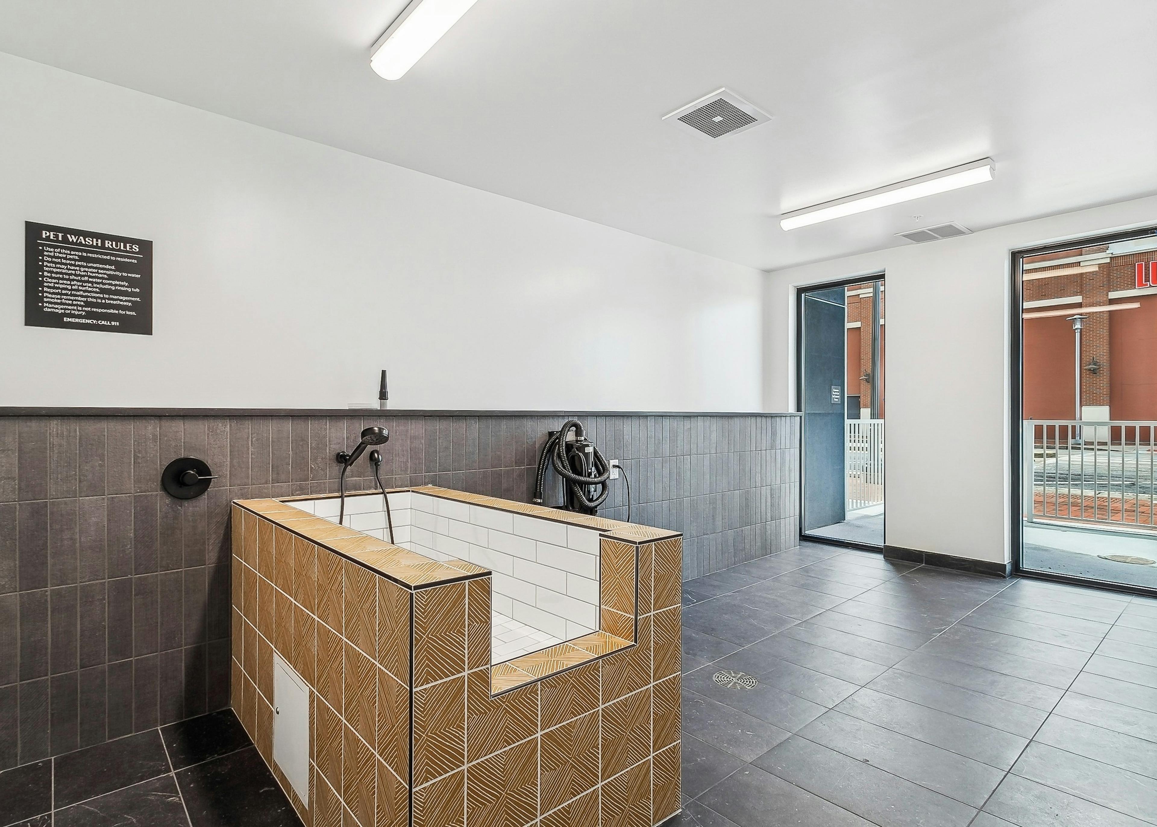 A pet washing station at AMLI Atlantic Station apartments with a tan and white tiled tub set on brown tiled floor and view to outside