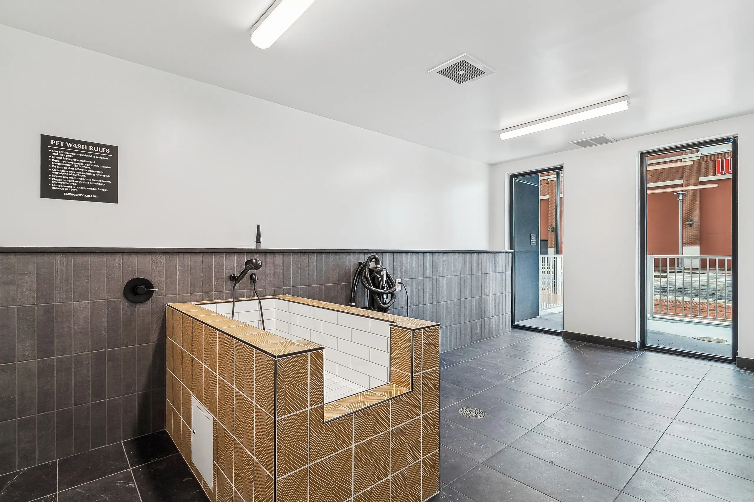 A pet washing station at AMLI Atlantic Station apartments with a tan and white tiled tub set on brown tiled floor and view to outside