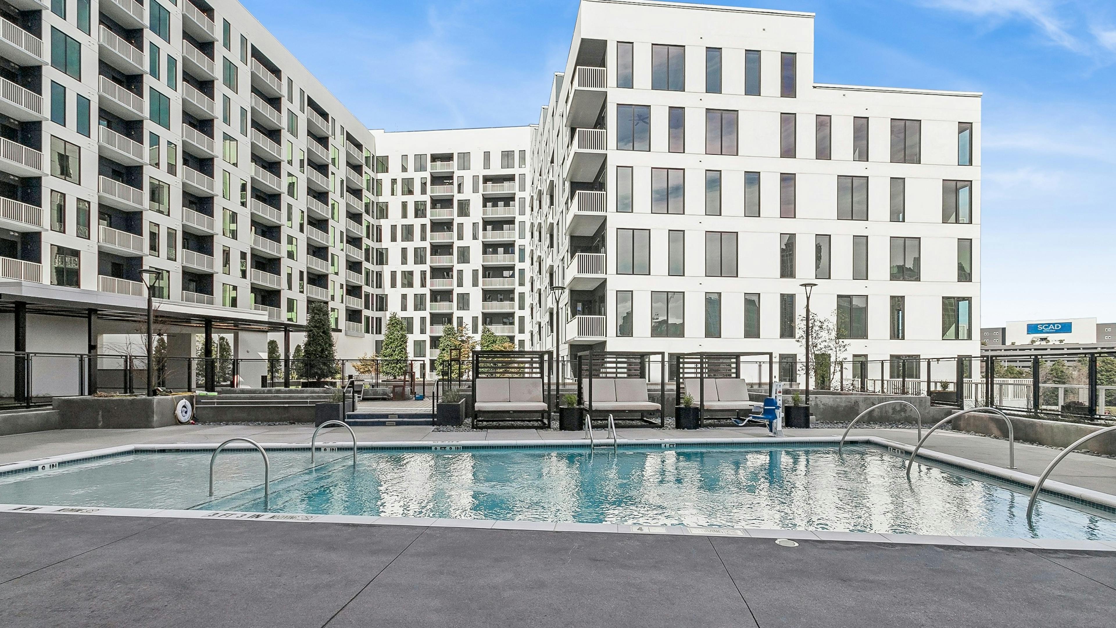 Outdoor pool area at AMLI Atlantic Station apartments with cabanas surrounded by white building with balconies