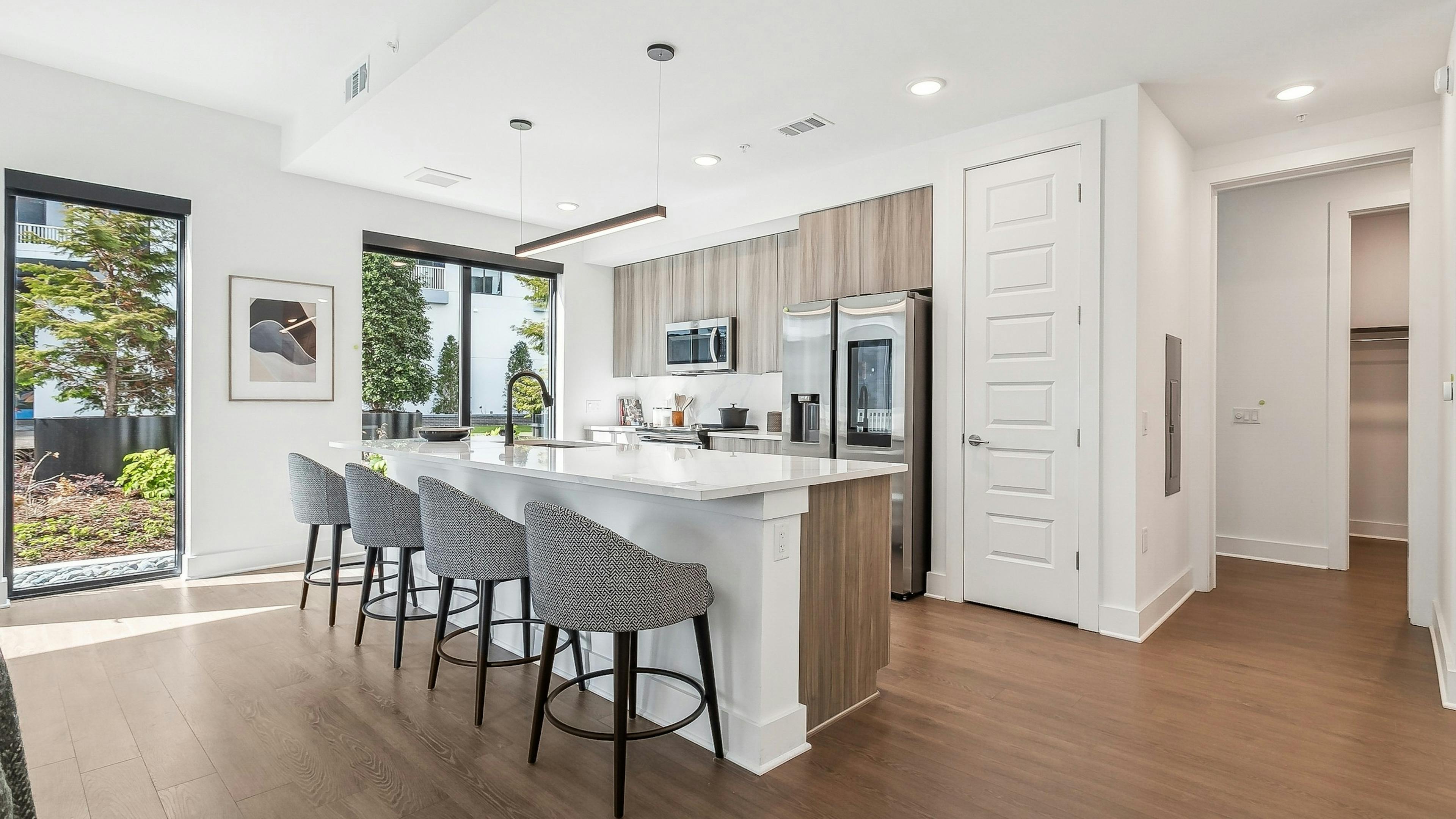 A kitchen at AMLI Atlantic Station with a wood floor and white island with four gray chairs and stainless steel appliances
