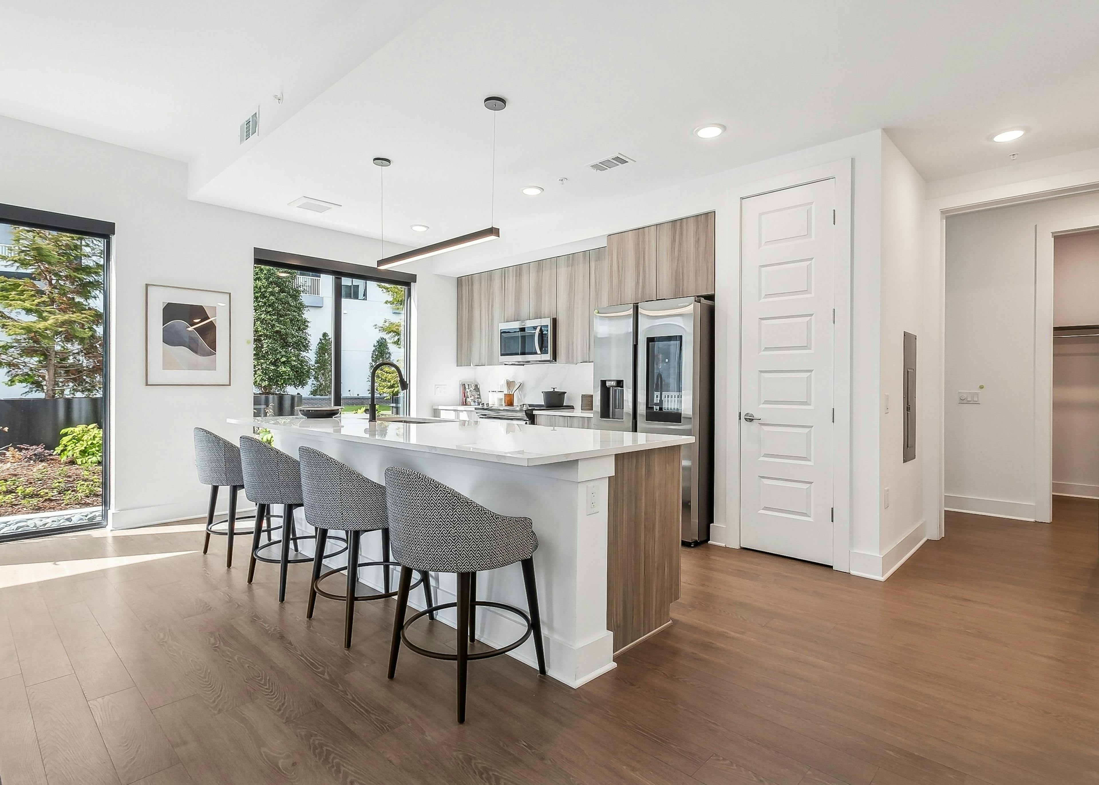 A kitchen at AMLI Atlantic Station with a wood floor and white island with four gray chairs and stainless steel appliances