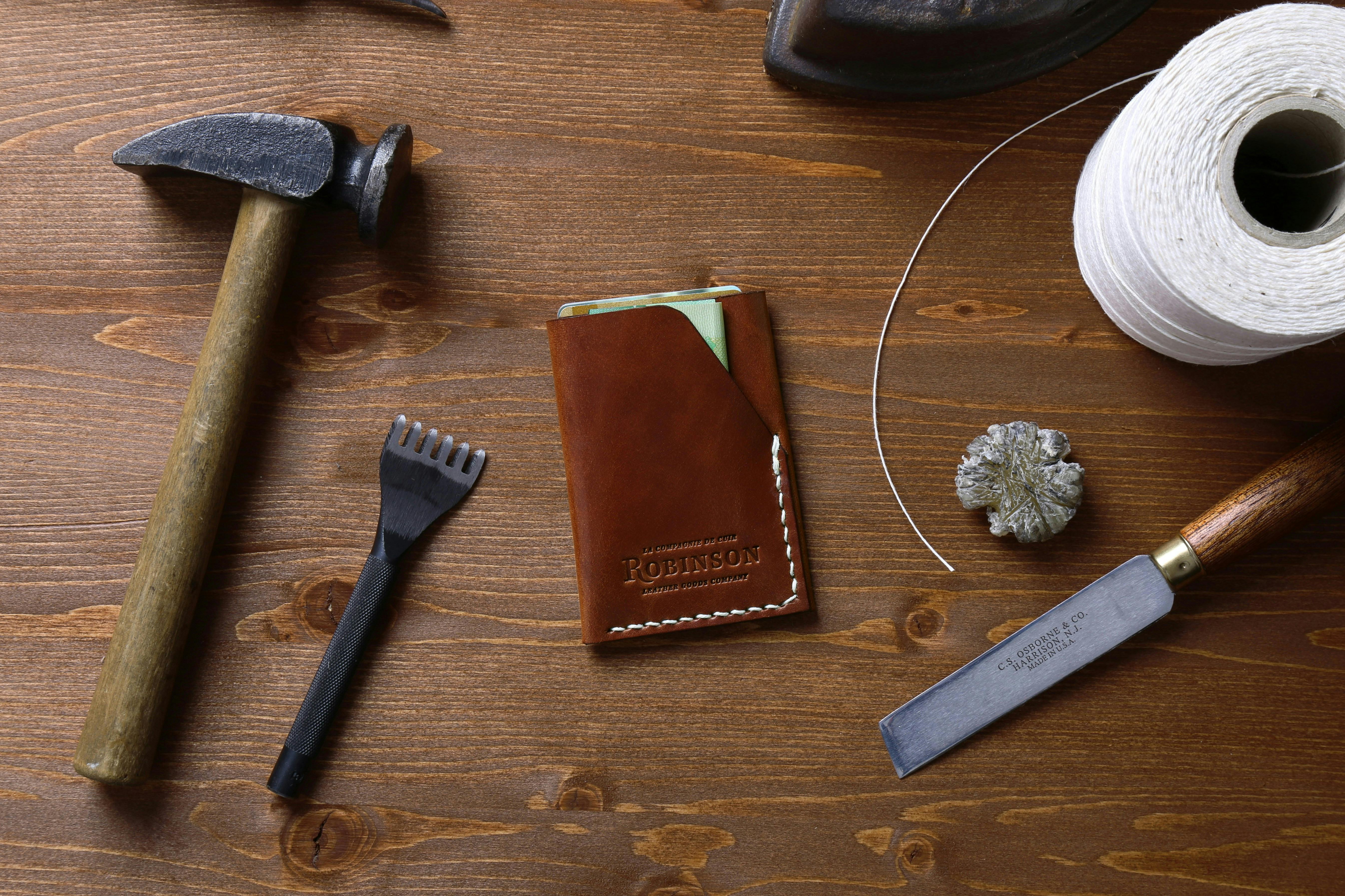 A brown leather wallet resting on a workbench beside some leather working tools