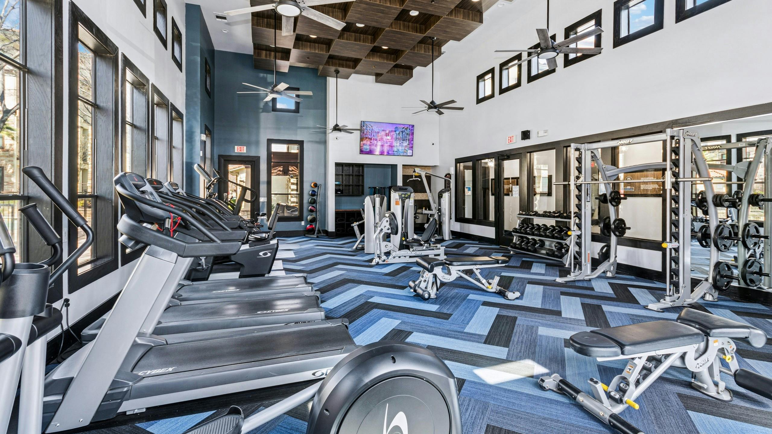 Fitness center with treadmills, weight machines and free weights on a blue geometric patterned floor at AMLI at Escena apartments