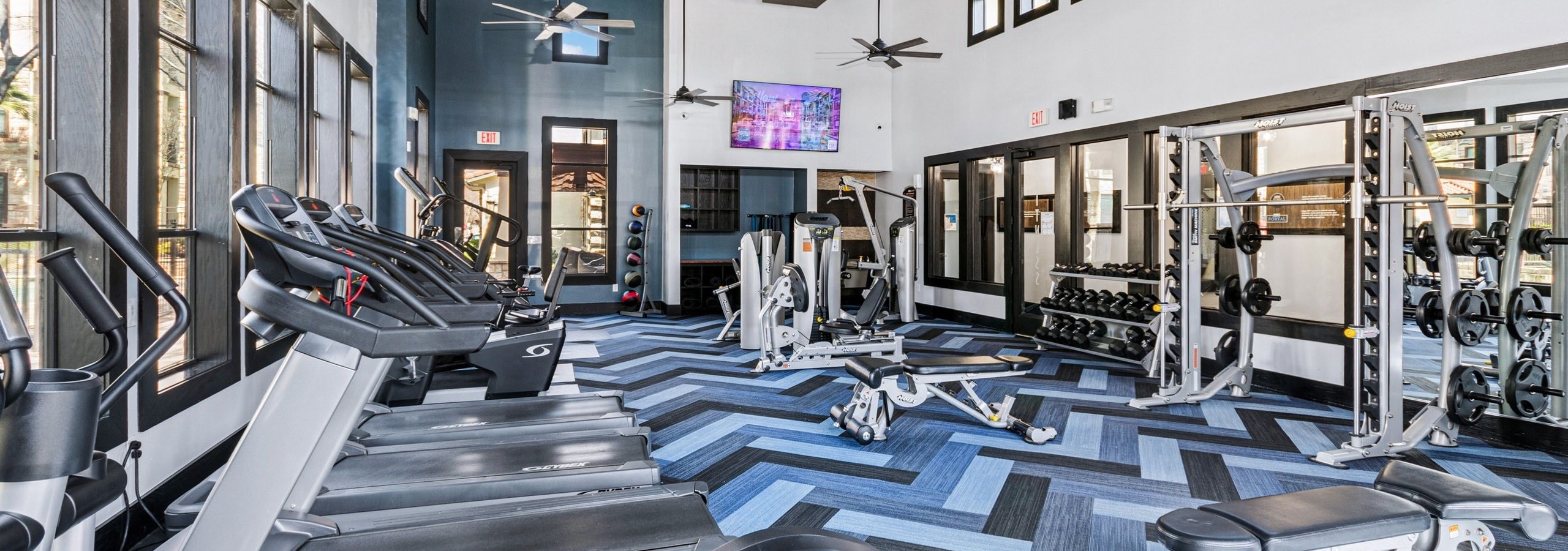 Fitness center with treadmills, weight machines and free weights on a blue geometric patterned floor at AMLI at Escena apartments