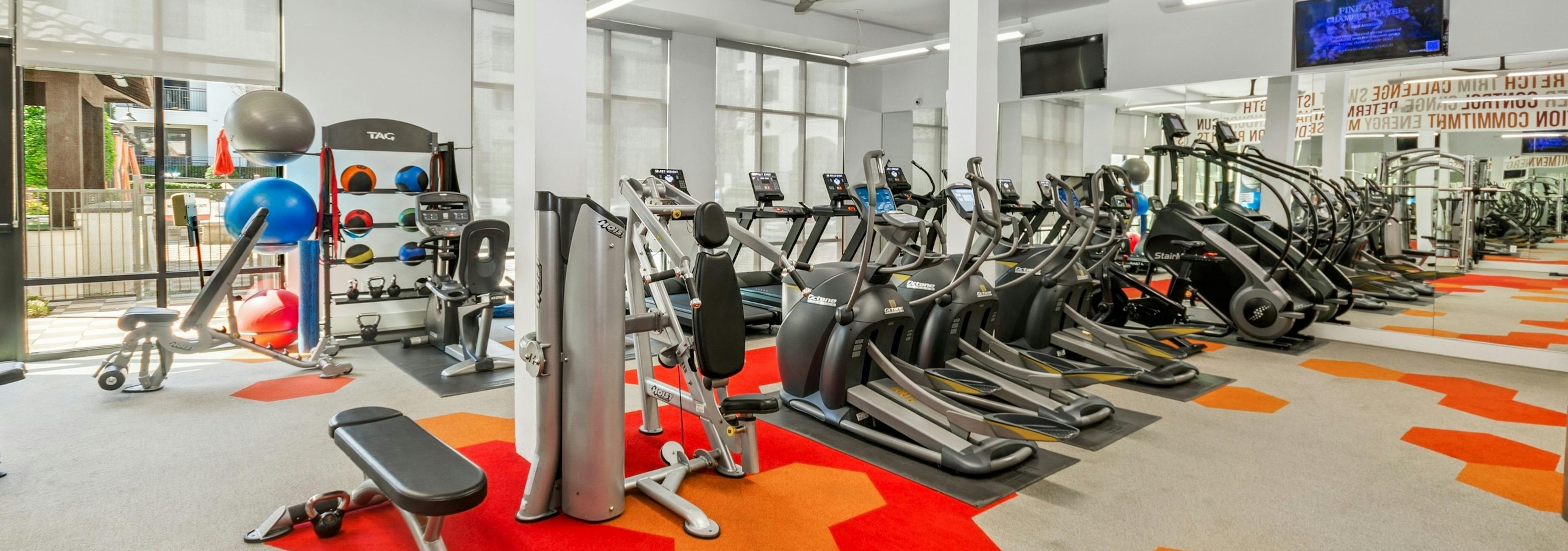 Modern gym at AMLI on Riverside with treadmills, ellipticals, and weight machines with a bright red and orange hexagonal patterned floor