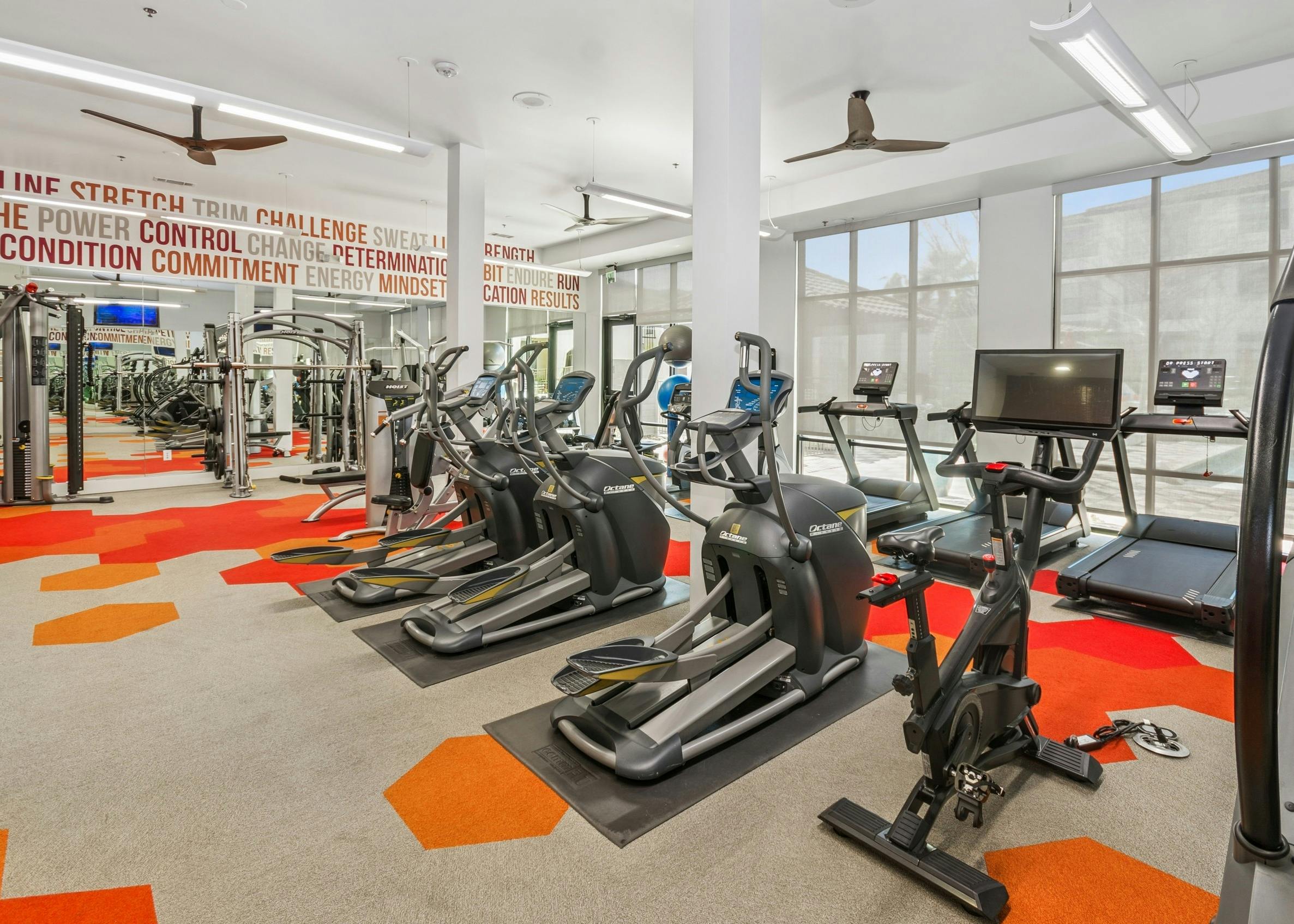 Exercise equipment at the AMLI on Riverside fitness center with geometric pattern flooring, and motivational words on the walls