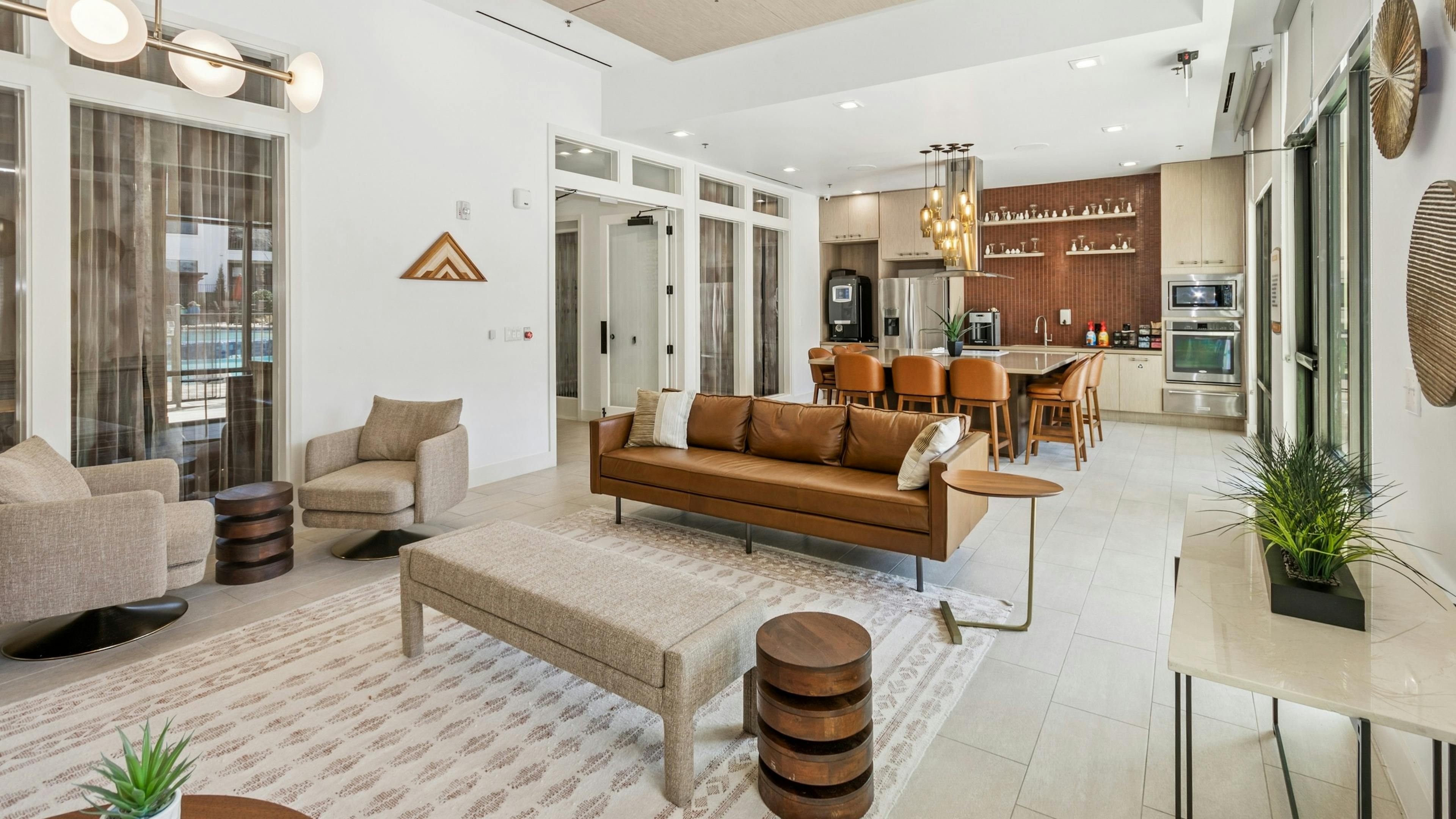 Resident lounge with brown leather couch and beige swivel chairs adjacent to resident kitchen at AMLI on Riverside apartments