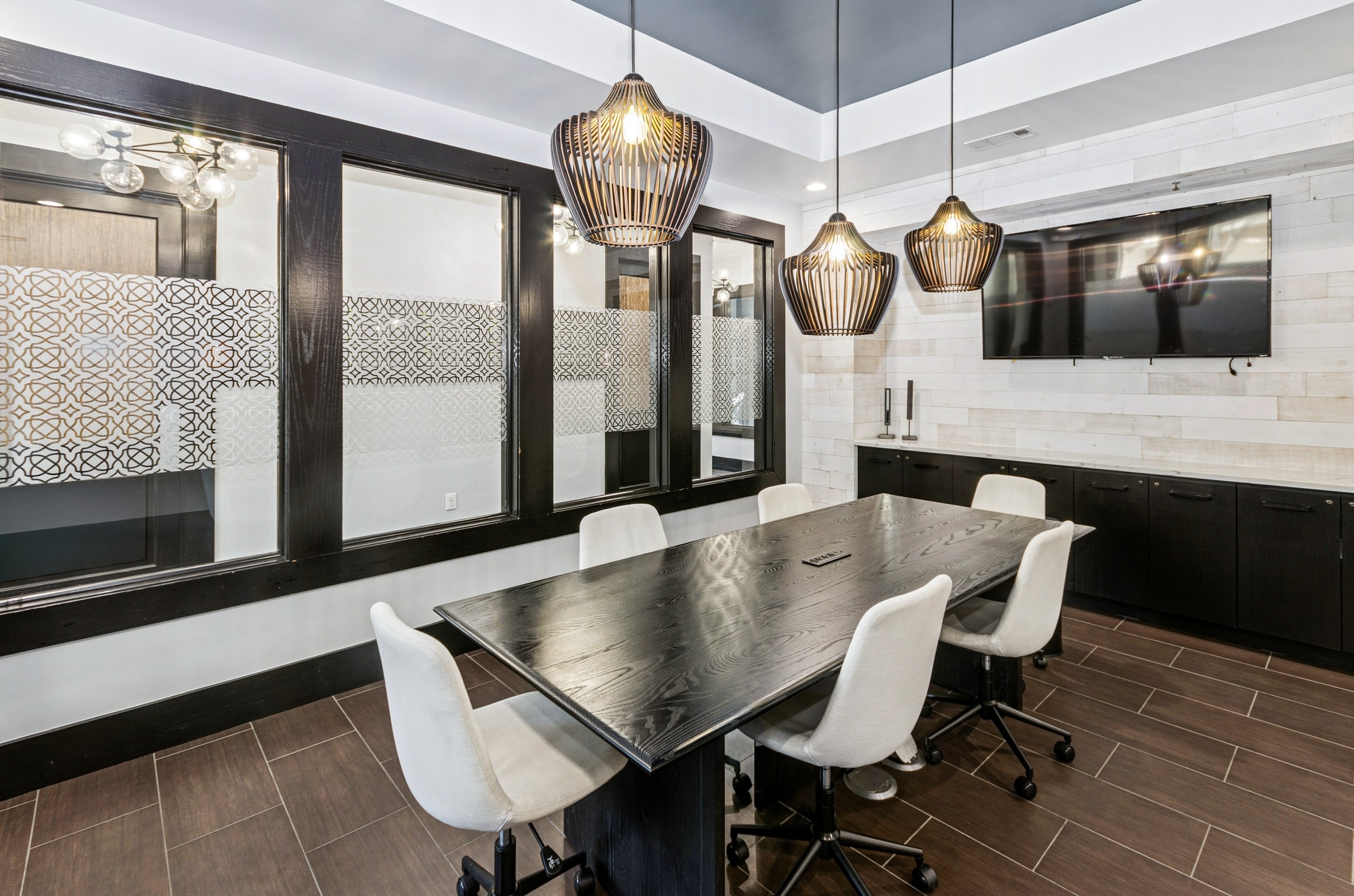 Conference room at AMLI at Escena with a large wood table, 6 white swivel chairs, a wall mounted TV and wall of windows