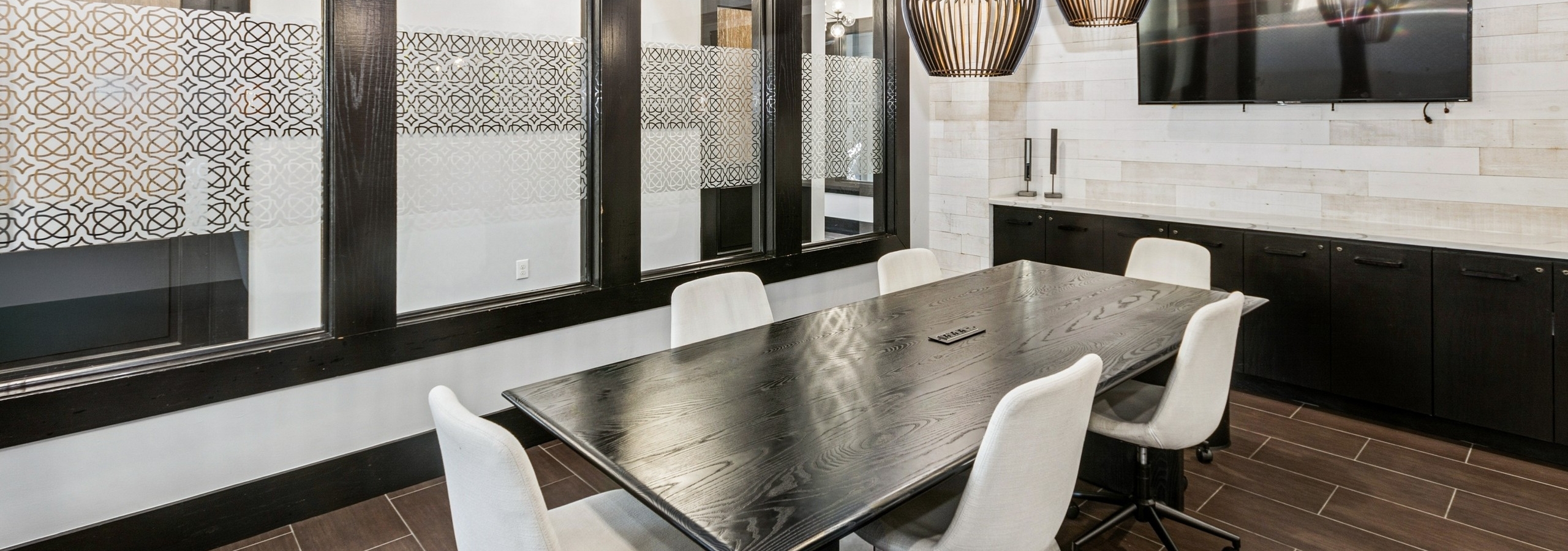 Conference room at AMLI at Escena with a large wood table, 6 white swivel chairs, a wall mounted TV and wall of windows