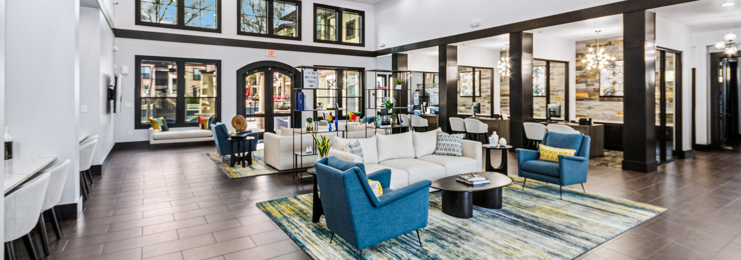 AMLI at Escena apartments leasing office and clubhouse with bright blue chairs, beige sofas, colorful rug and large windows