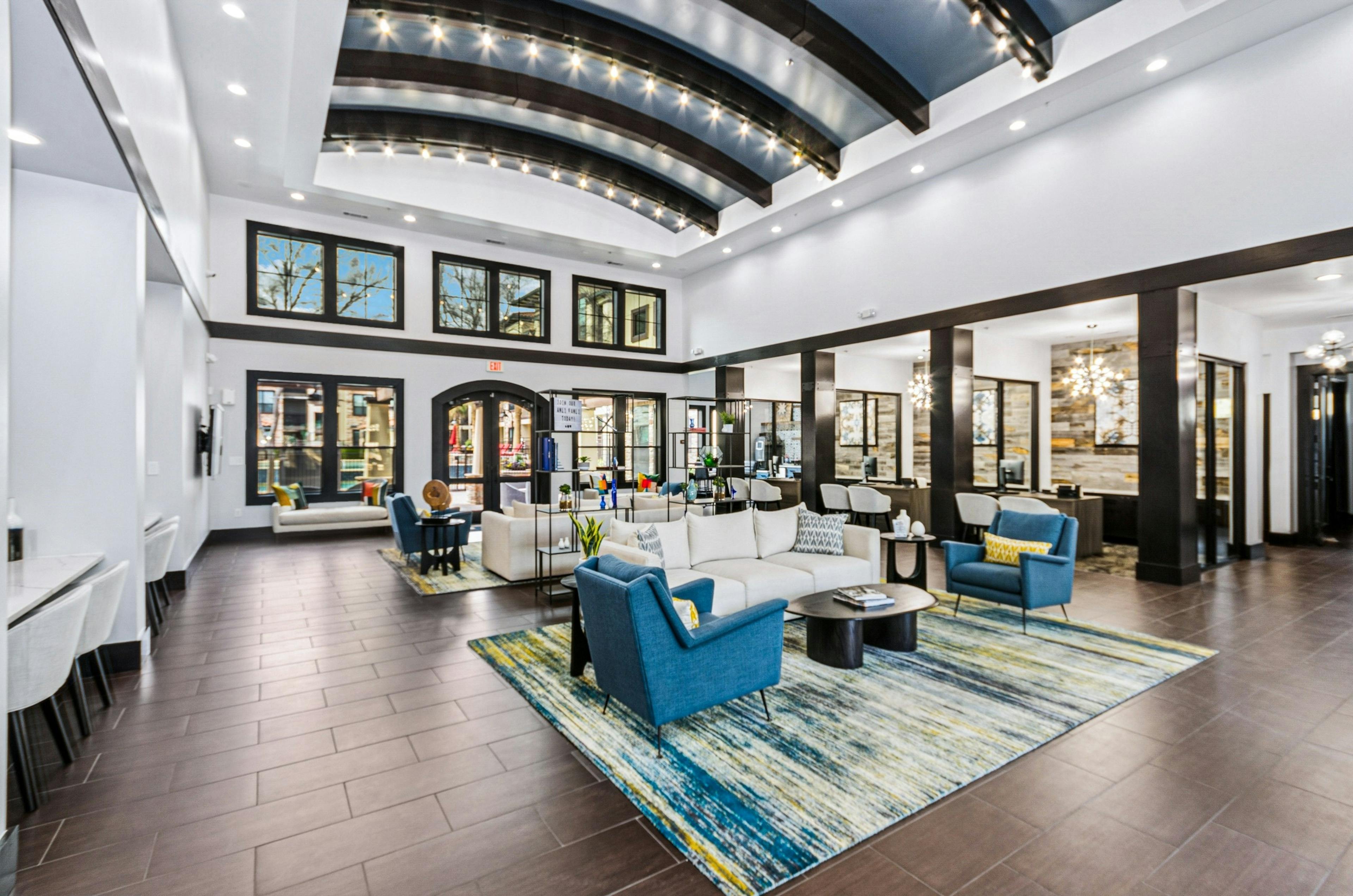 AMLI at Escena apartments leasing office and clubhouse with bright blue chairs, beige sofas, colorful rug and large windows