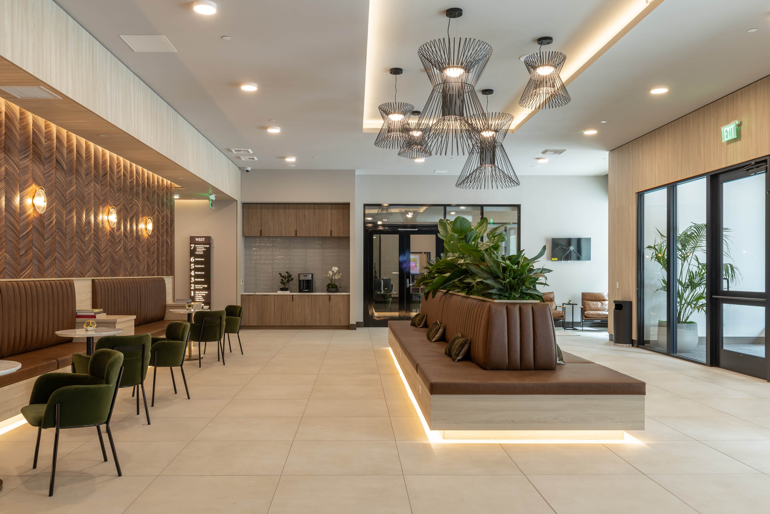 West building lobby with pendant lighting, leather lounge seating, a coffee bar, and a wood-paneled feature wall.