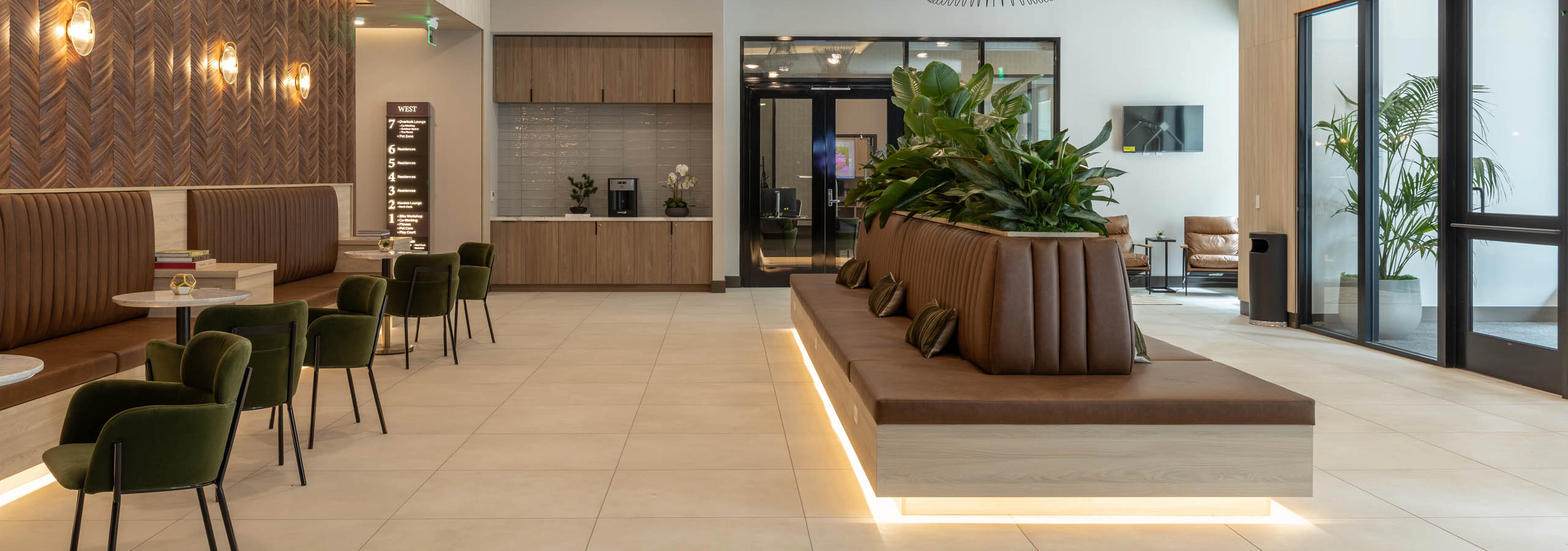 West building lobby with pendant lighting, leather lounge seating, a coffee bar, and a wood-paneled feature wall.