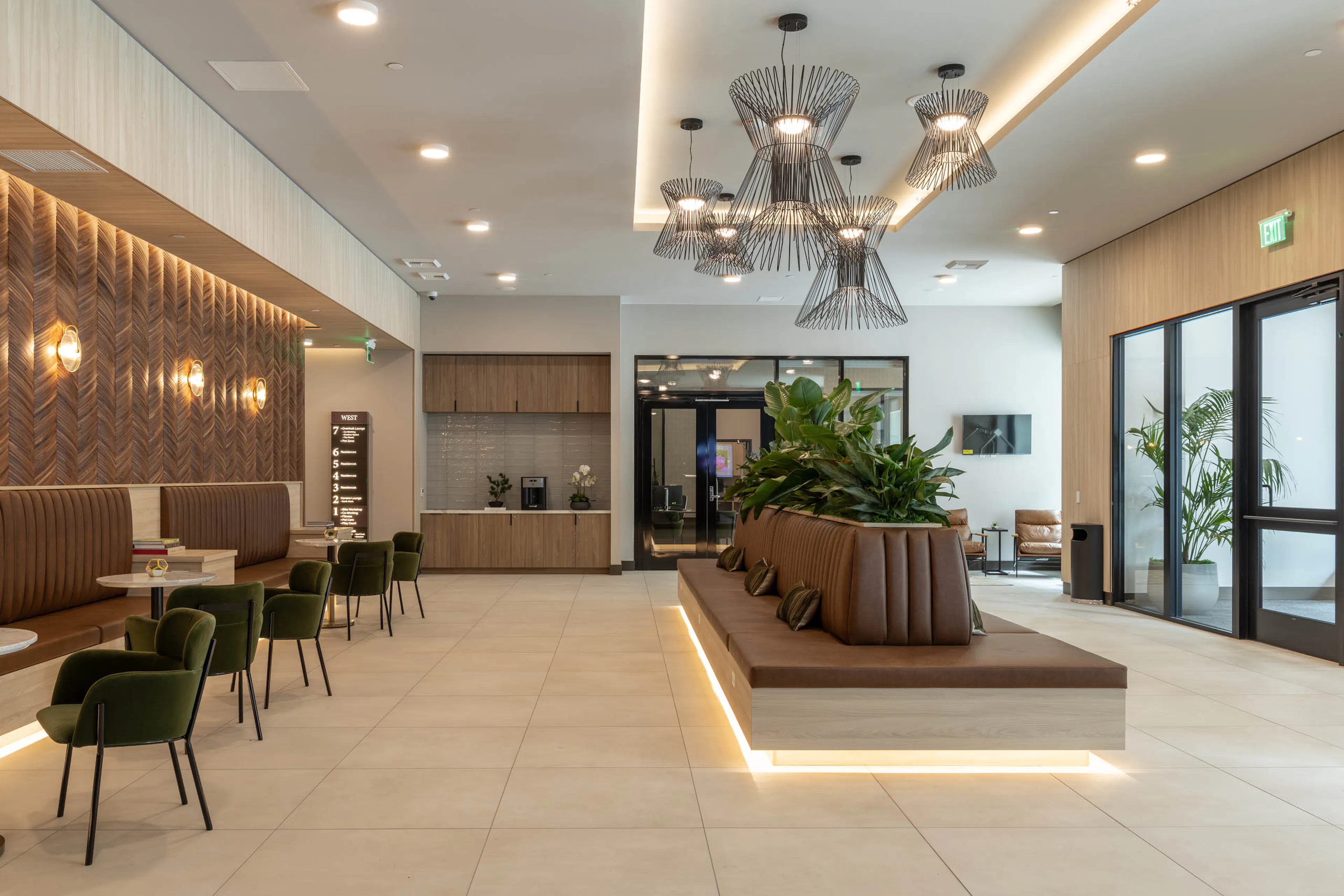 West building lobby with pendant lighting, leather lounge seating, a coffee bar, and a wood-paneled feature wall.