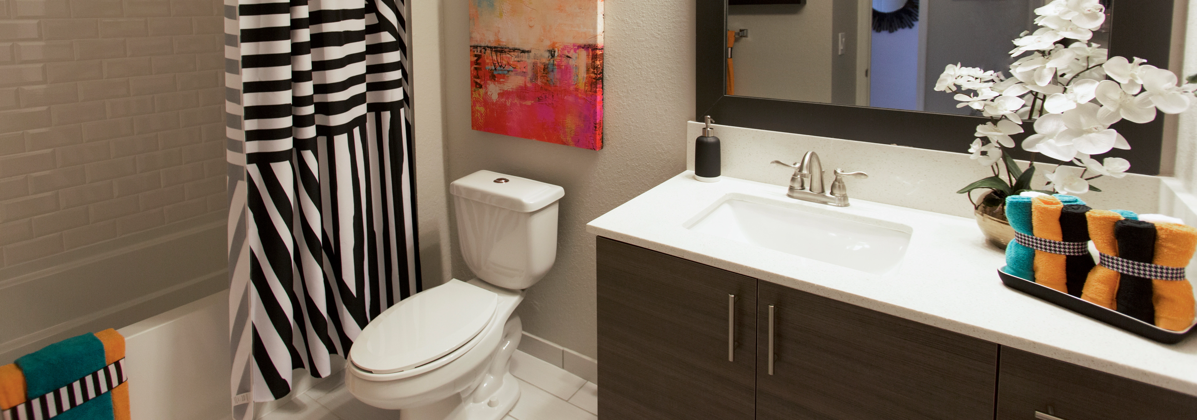 Interior view of bathroom at AMLI Dadeland apartments with single sink vanity, mirror and black and white shower curtain