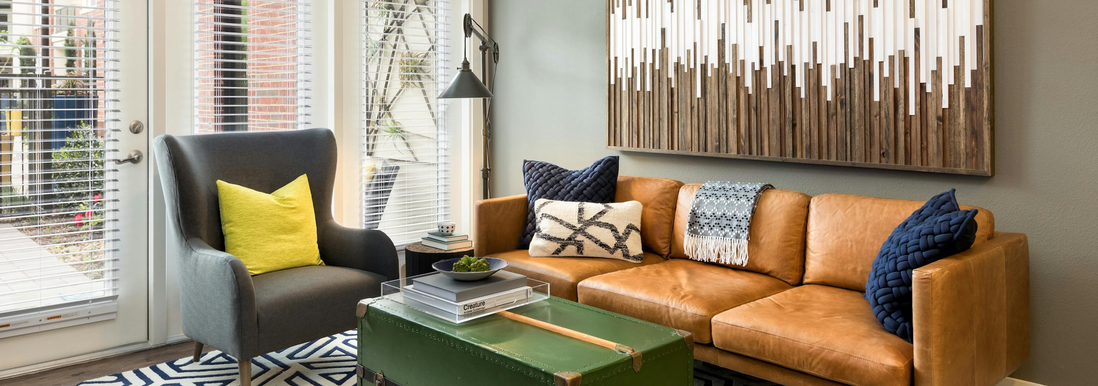 AMLI Frisco Crossing living room with brown leather couch, grey armchair and wall of windows with glass patio door