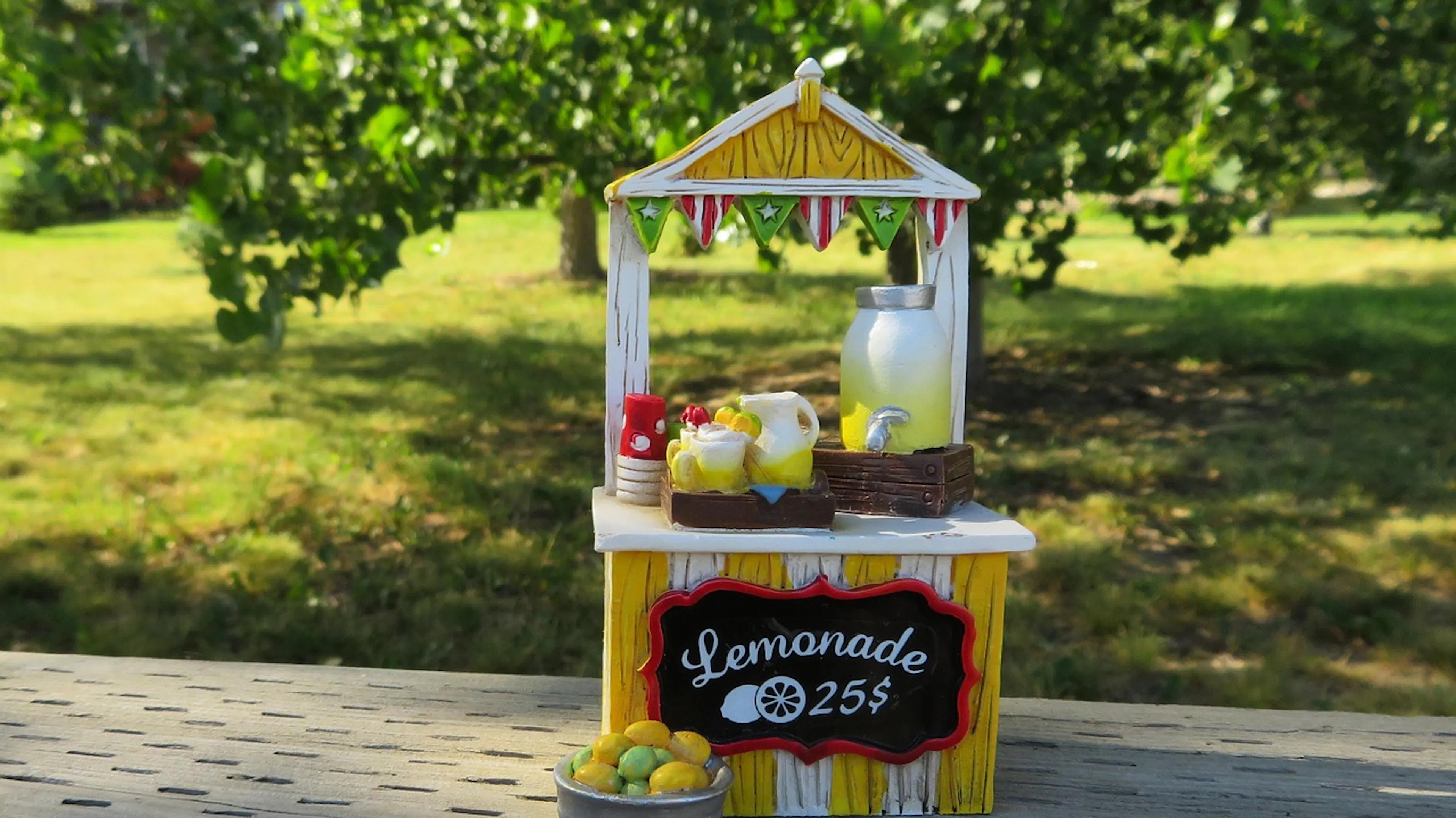 Yellow and white striped childrens lemonade stand with green grass and trees