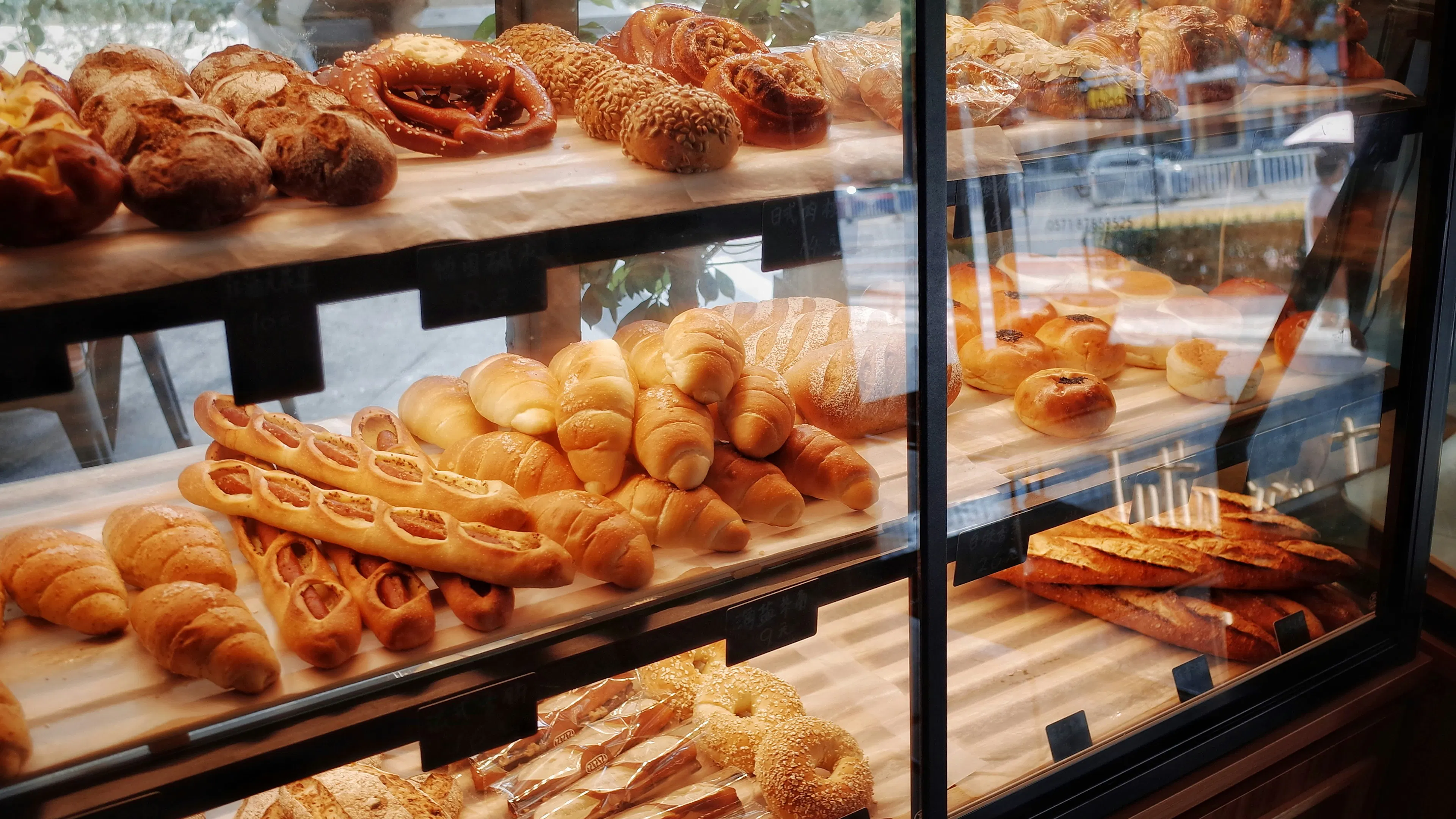 A bakery window display case with pastries like croissants, baguettes, muffins and bagels