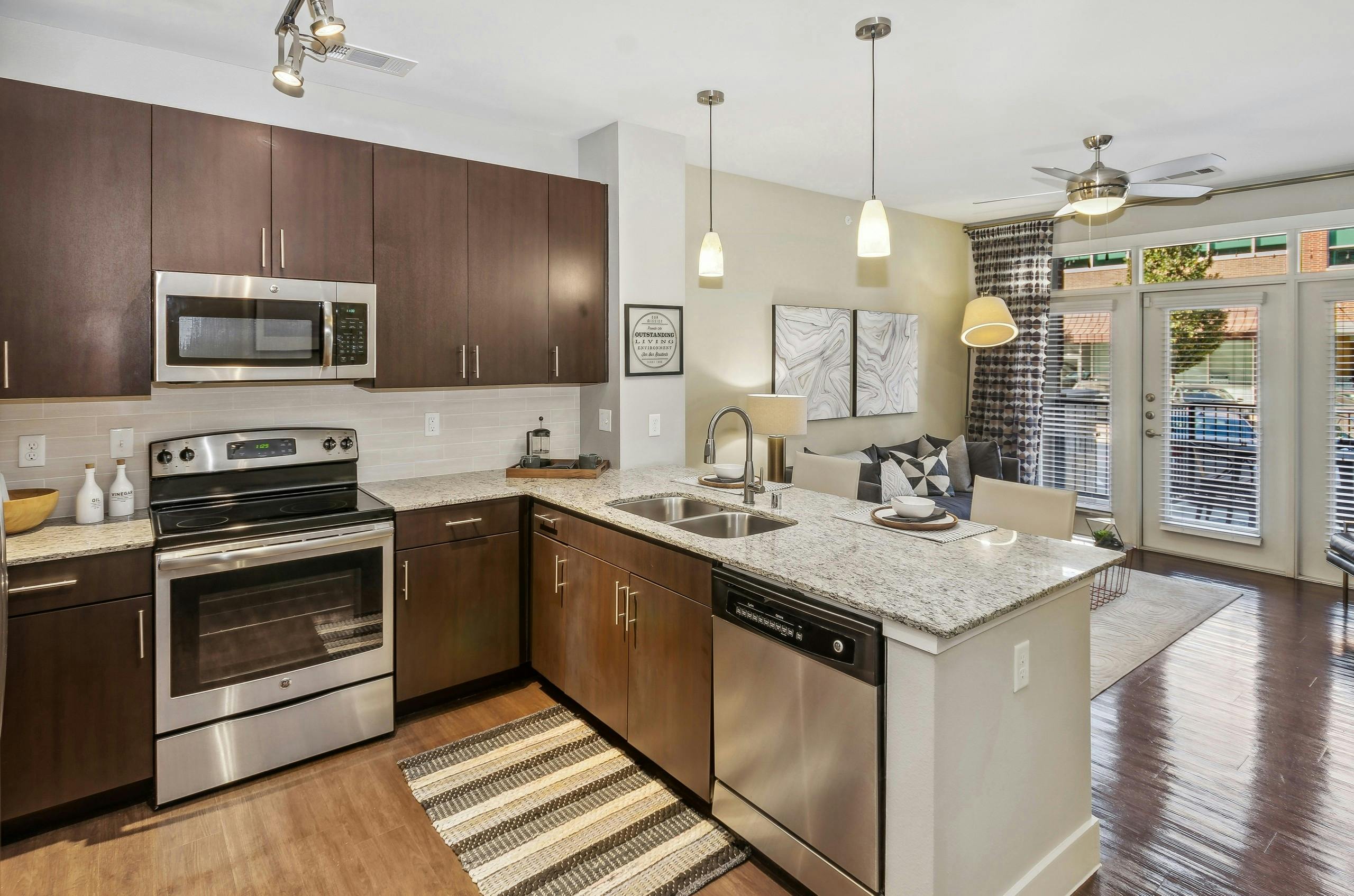 Kitchen at AMLI West Plano with stainless steel appliances and dark brown cabinets and island peninsula with hanging pendant lights above