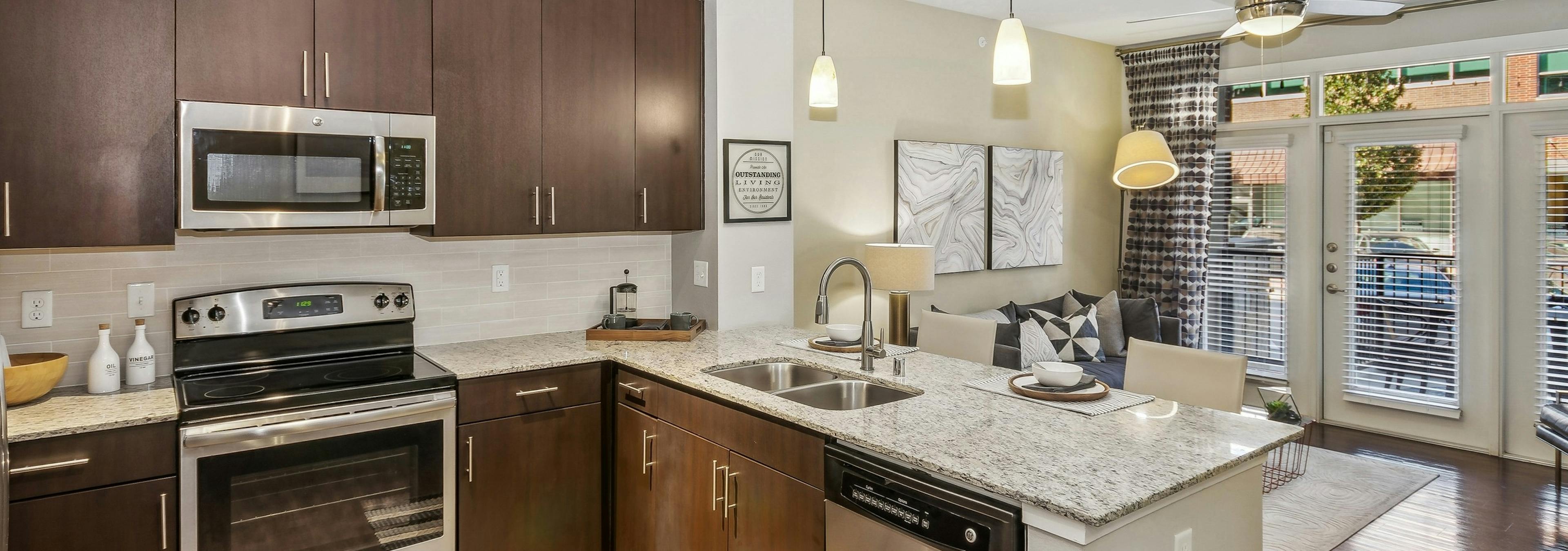 Kitchen at AMLI West Plano with stainless steel appliances and dark brown cabinets and island peninsula with hanging pendant lights above