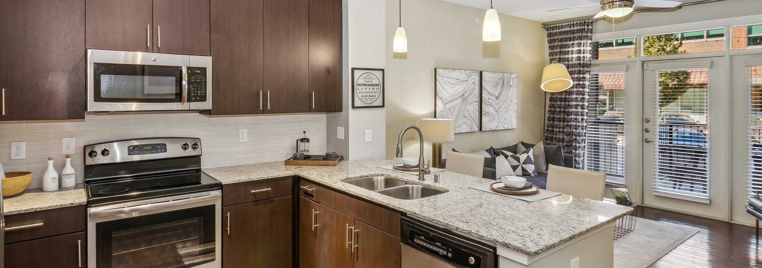 Kitchen at AMLI West Plano with stainless steel appliances and dark brown cabinets and island peninsula with hanging pendant lights above