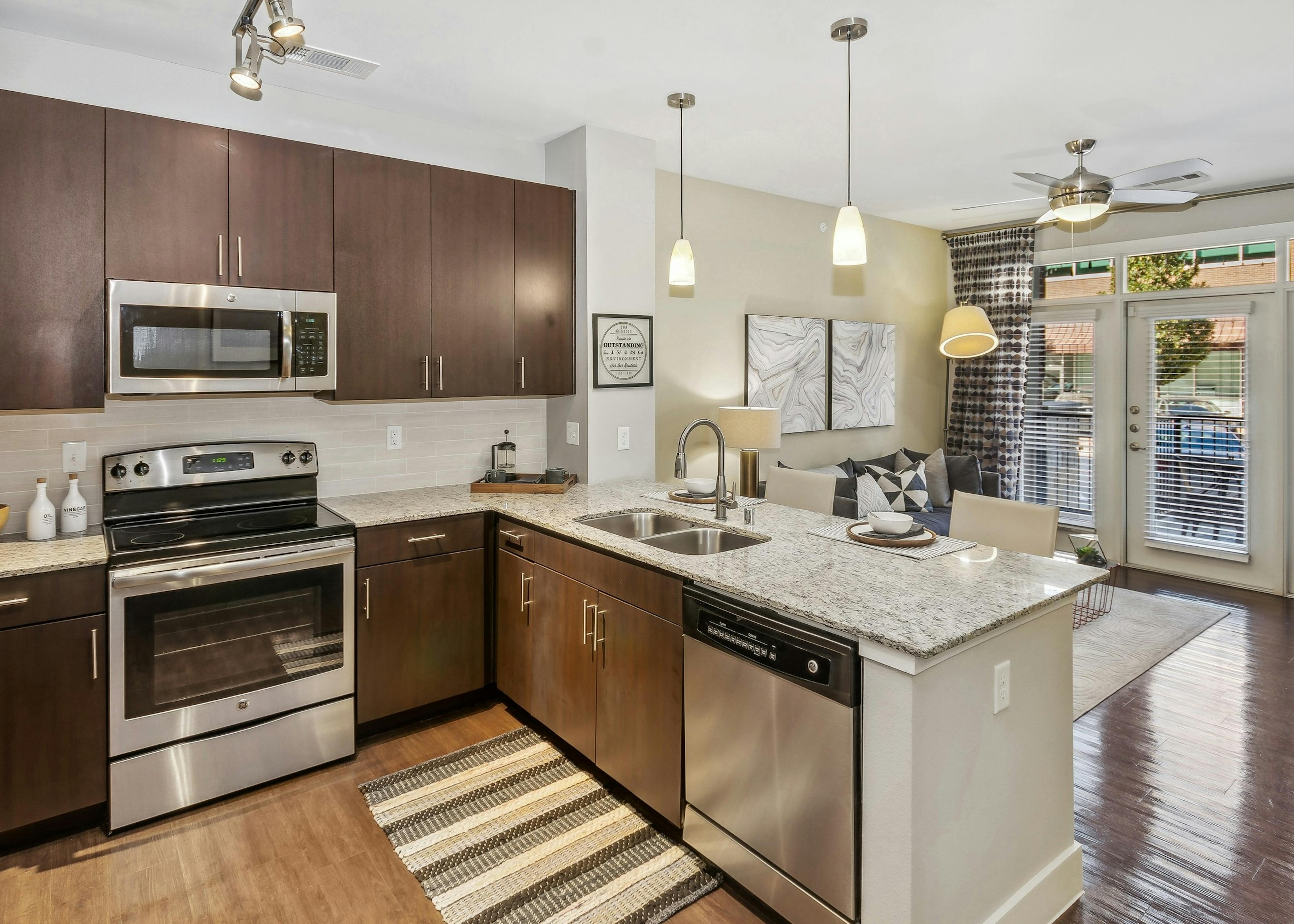 Kitchen at AMLI West Plano with stainless steel appliances and dark brown cabinets and island peninsula with hanging pendant lights above