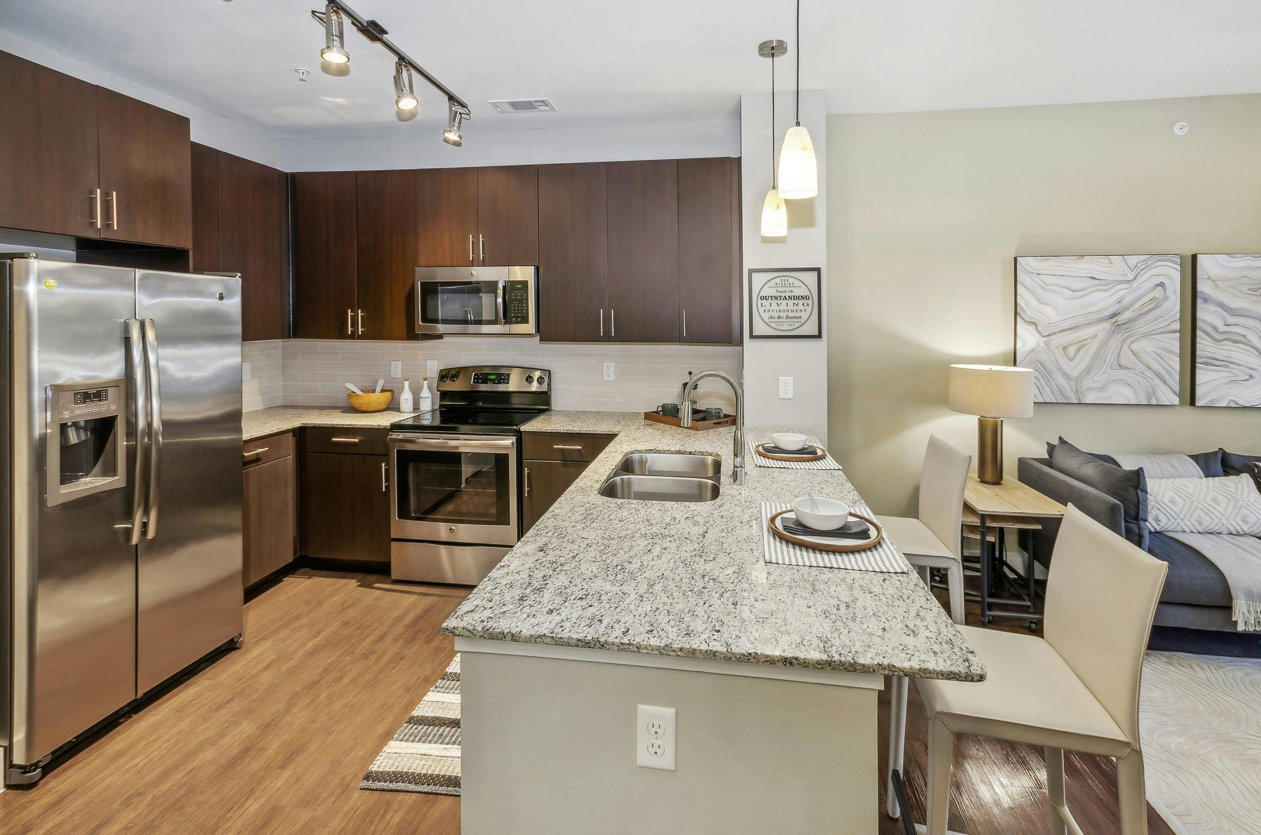 AMLI West Plano apartment kitchen with granite countertops and espresso wood cabinets and stainless appliances adjacent to the living room