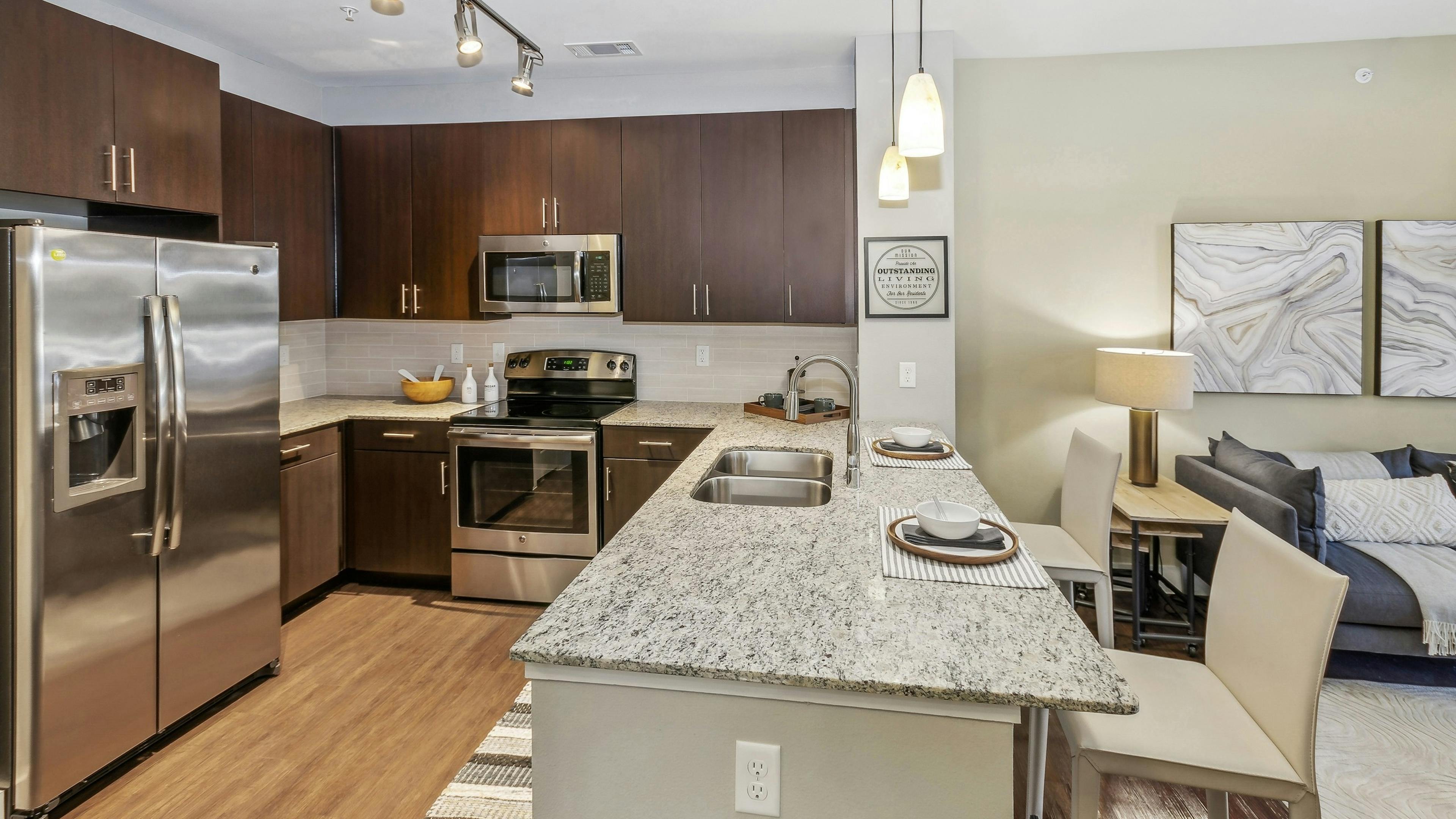 AMLI West Plano apartment kitchen with granite countertops and espresso wood cabinets and stainless appliances adjacent to the living room 