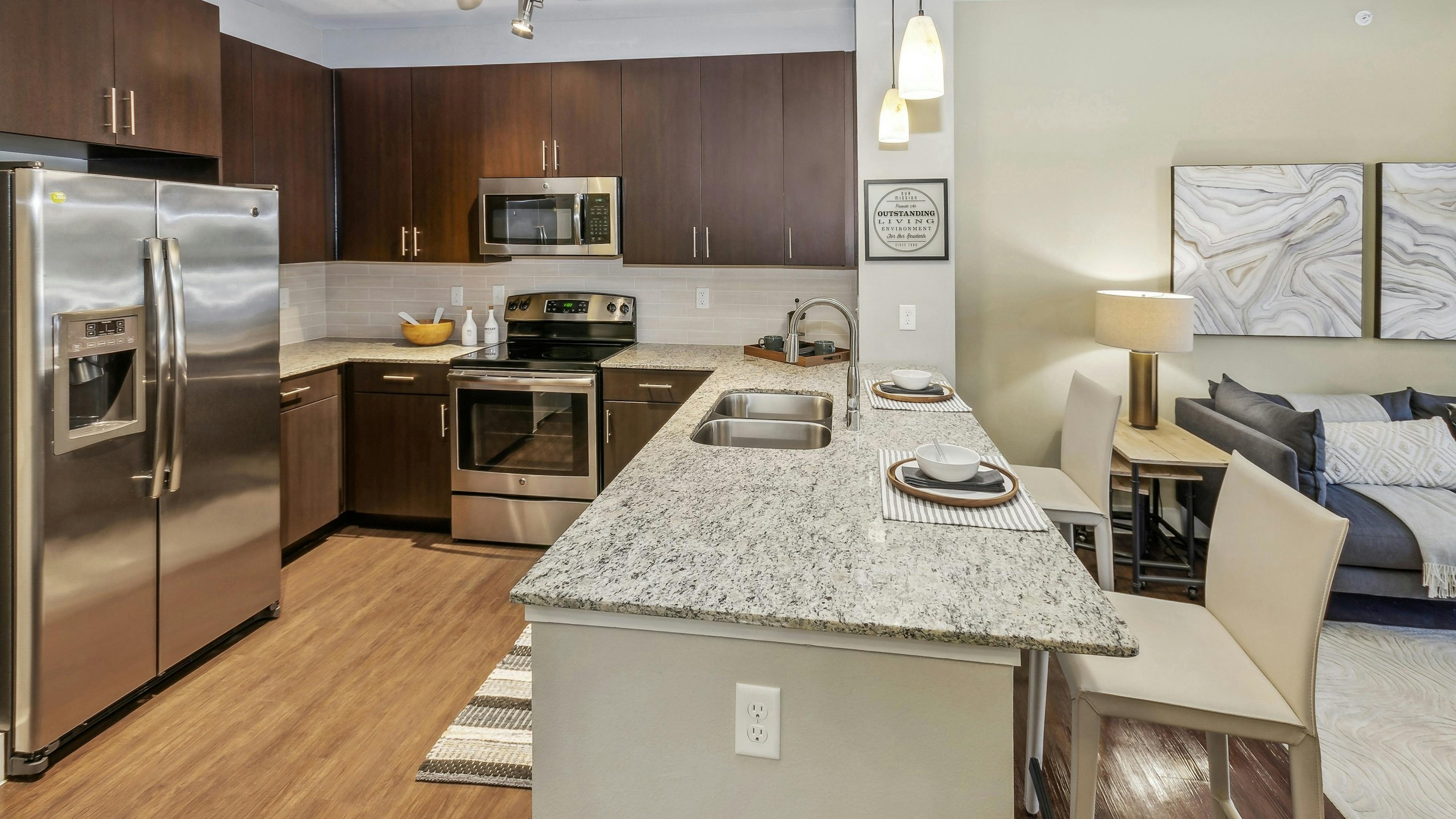 AMLI West Plano apartment kitchen with granite countertops and espresso wood cabinets and stainless appliances adjacent to the living room 